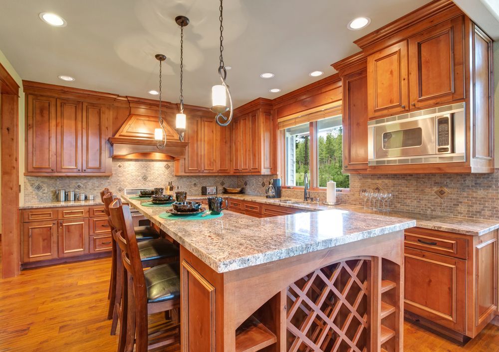 Wooden kitchen with granite countertops, island with wine rack, pendant lights, and stainless steel microwave.
