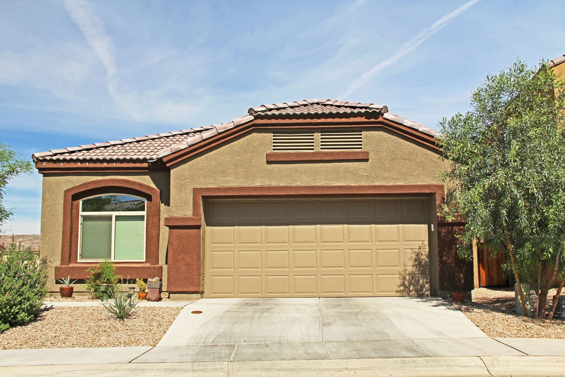 Tan stucco home with a brown garage door and trim, set against a blue sky.