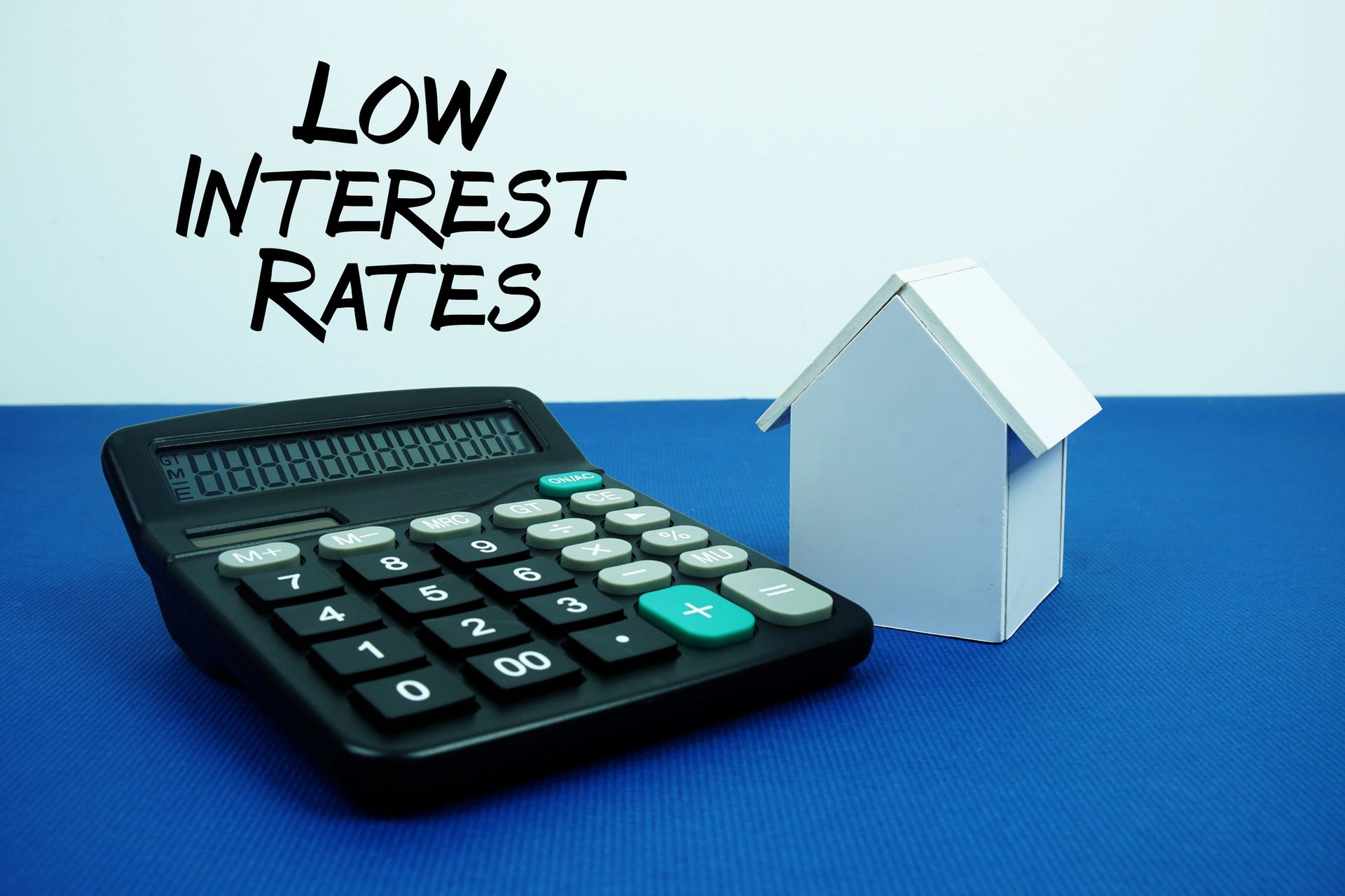 Calculator next to a white paper house on blue surface with text LOW INTEREST RATES.