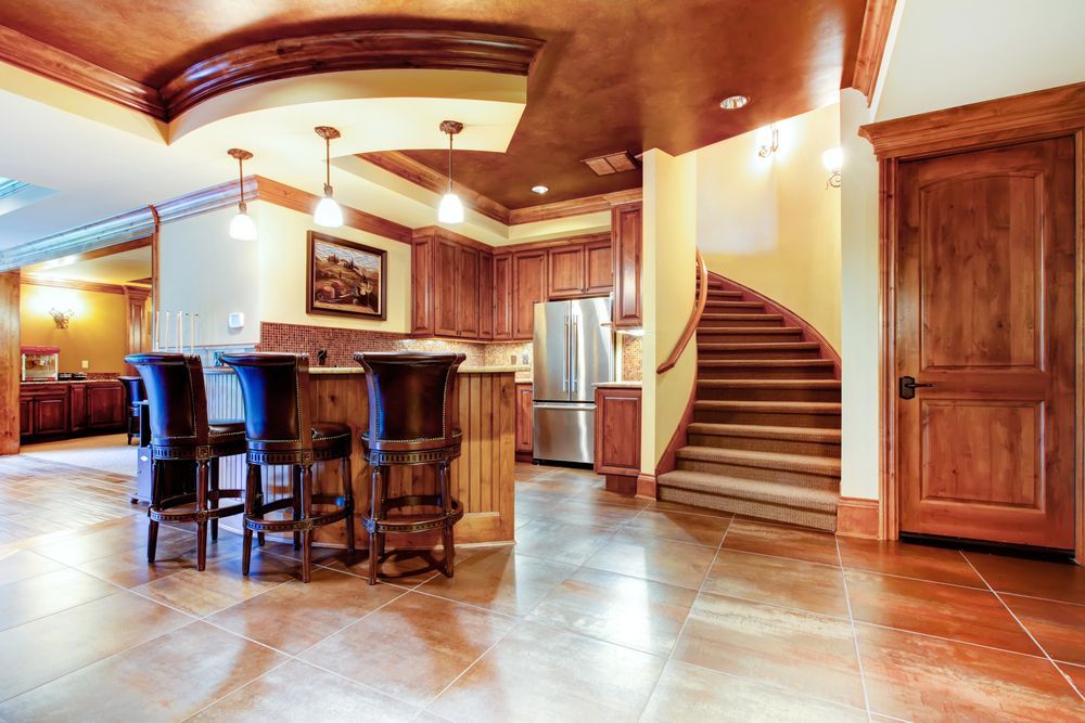 A finished basement with a kitchen, bar stools, and a wooden staircase.