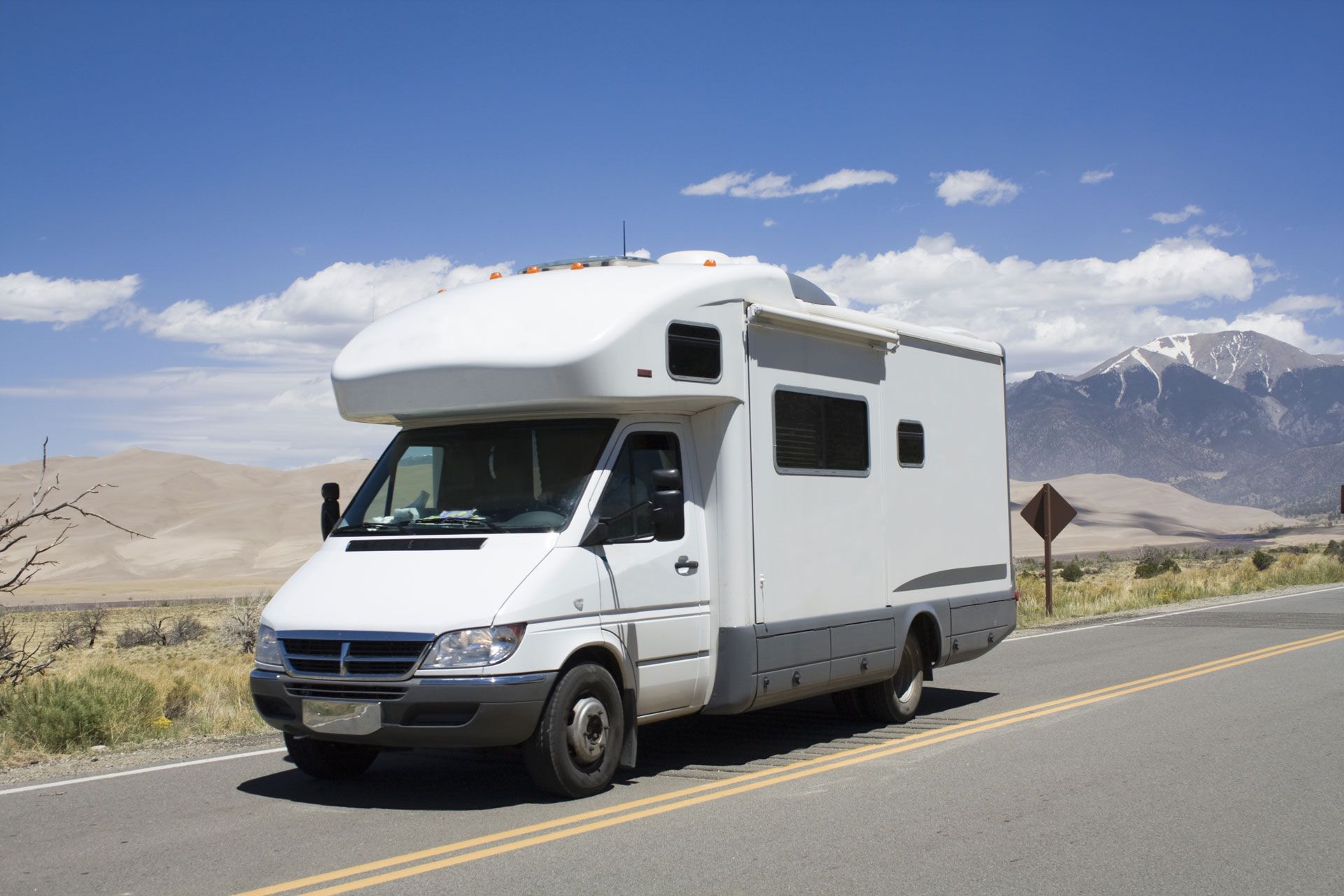A white rv is driving down a road with mountains in the background