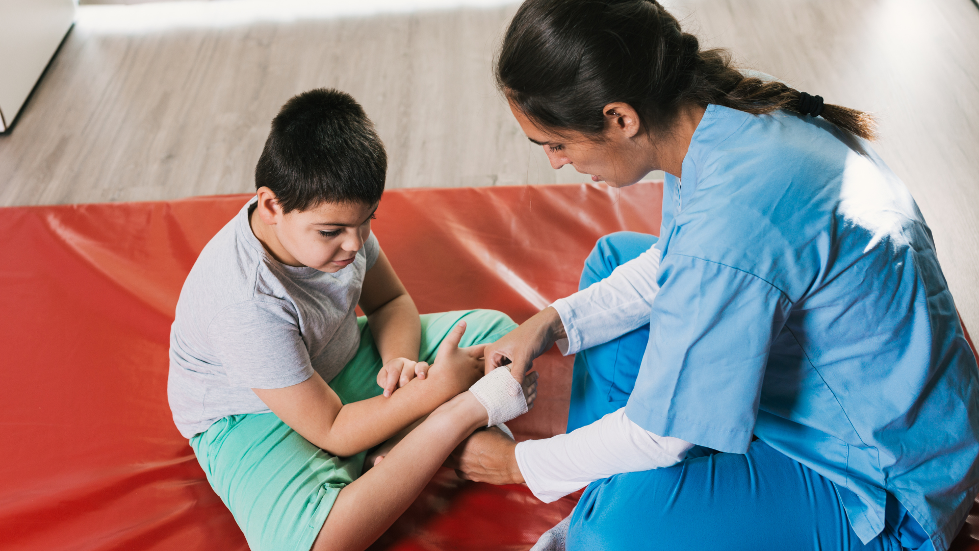 A nurse is bandaging a child 's leg on a mat.