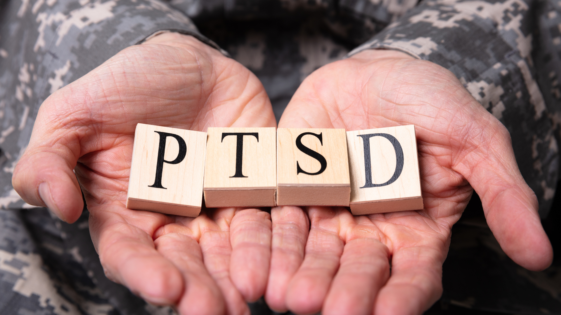 A person in a military uniform is holding wooden blocks that spell out the word ptsd.