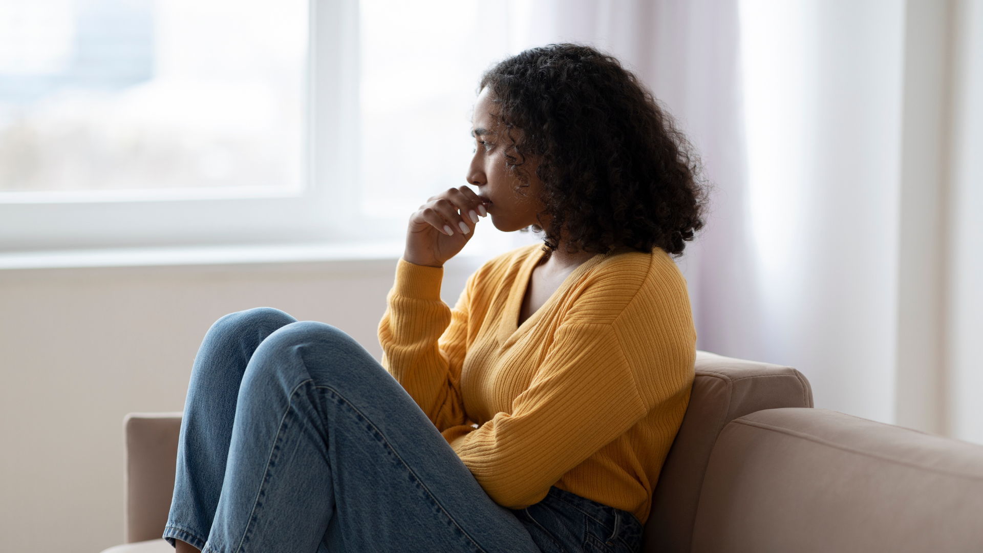 A woman is sitting on a couch looking out the window.