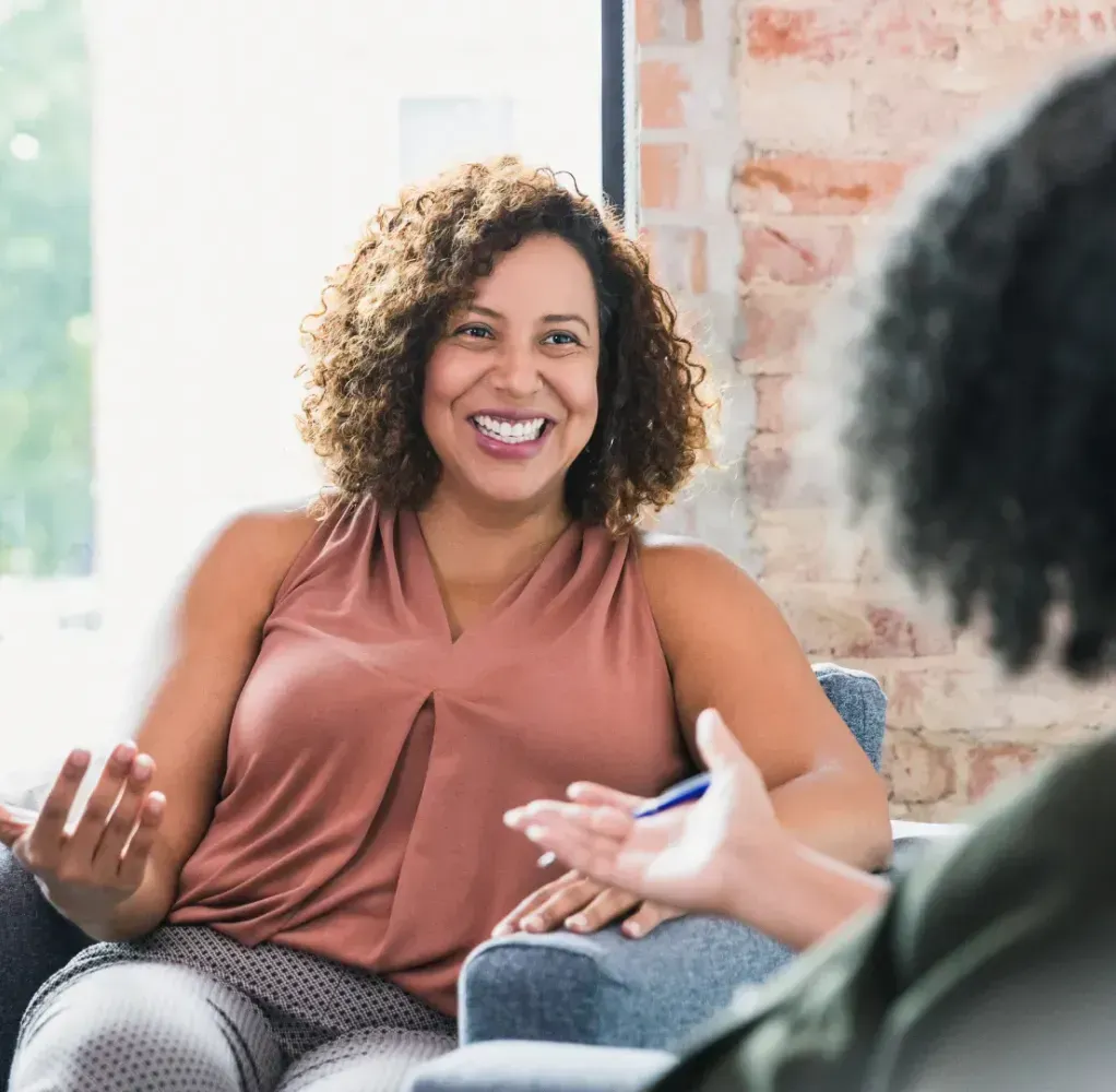 A woman is sitting in a chair talking to another woman.