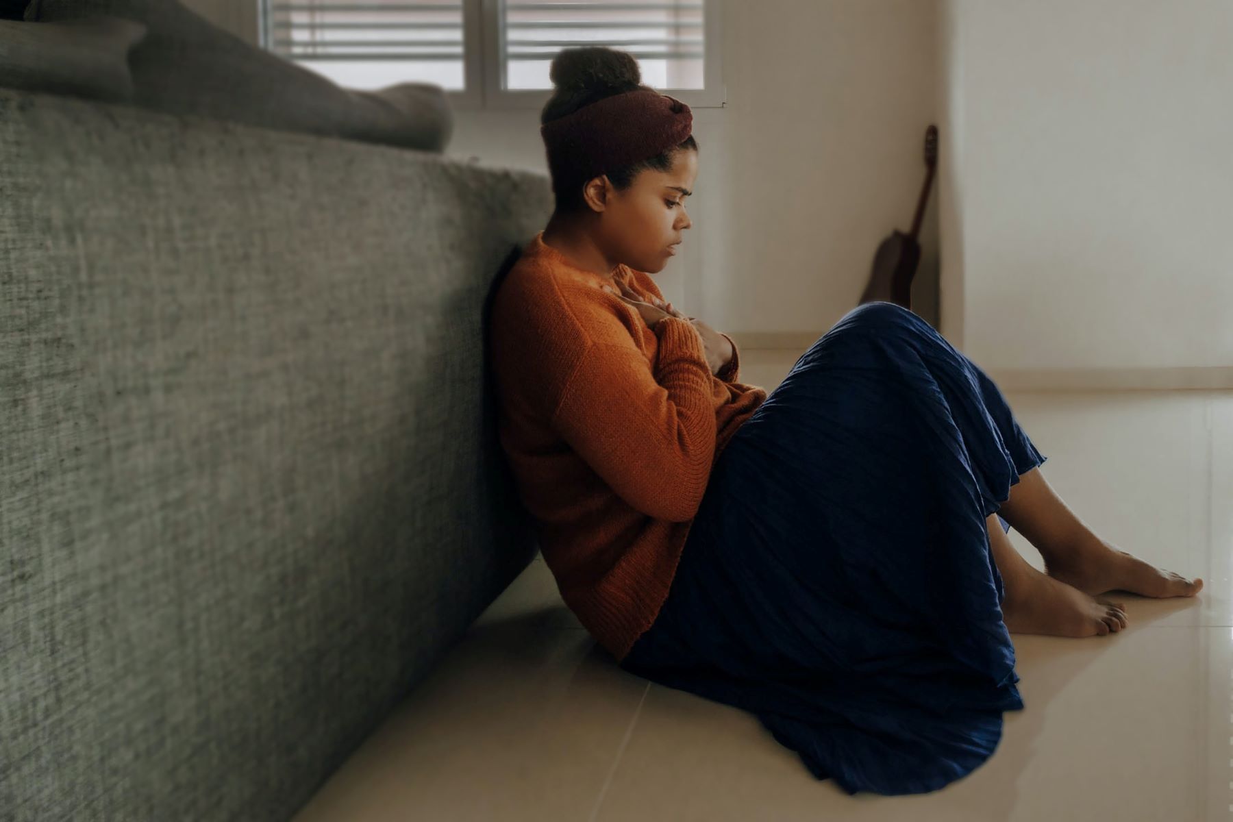 A woman is sitting on the floor leaning against a couch with chest pain.