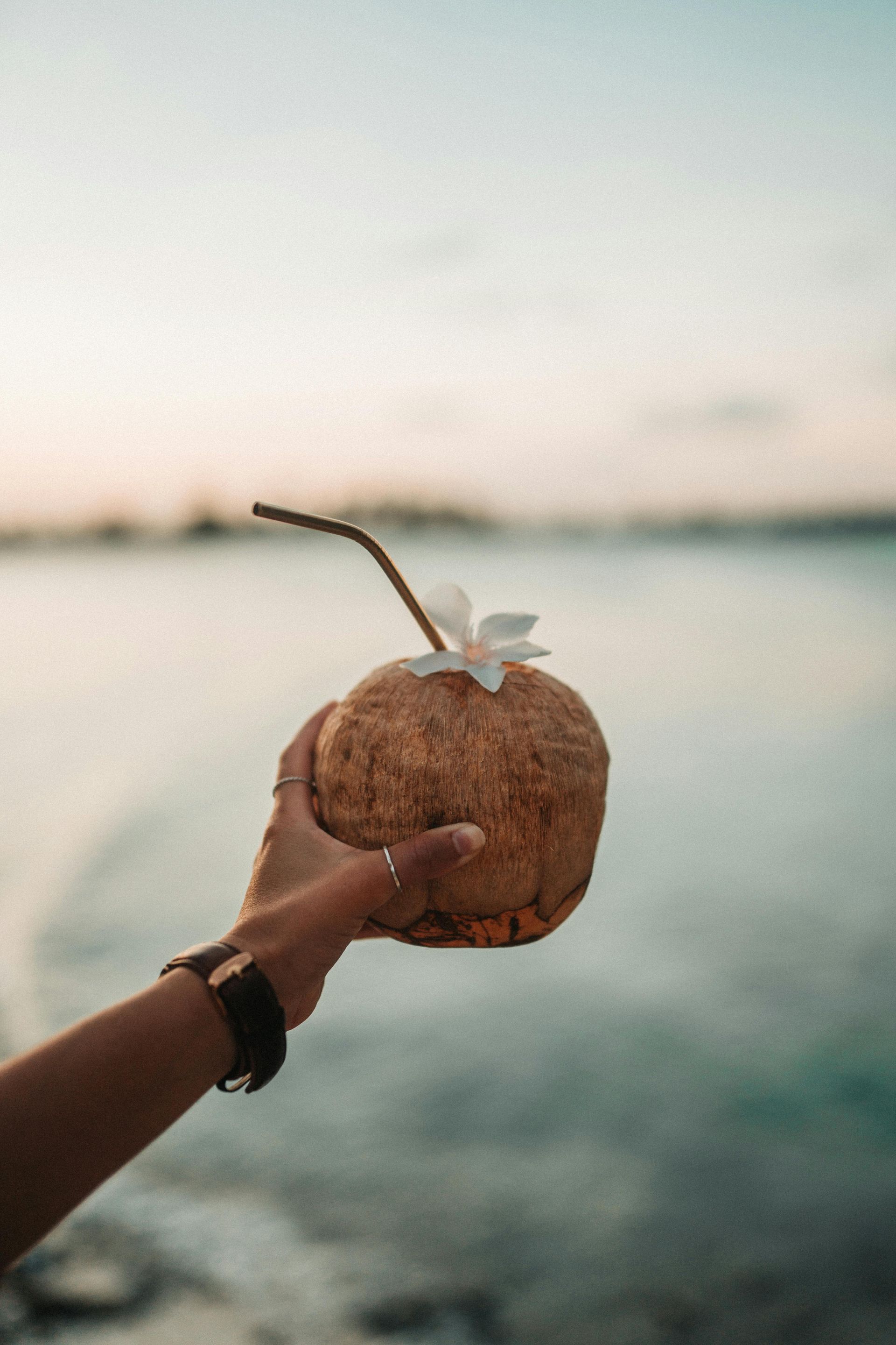 A person is holding a coconut with a straw in it.