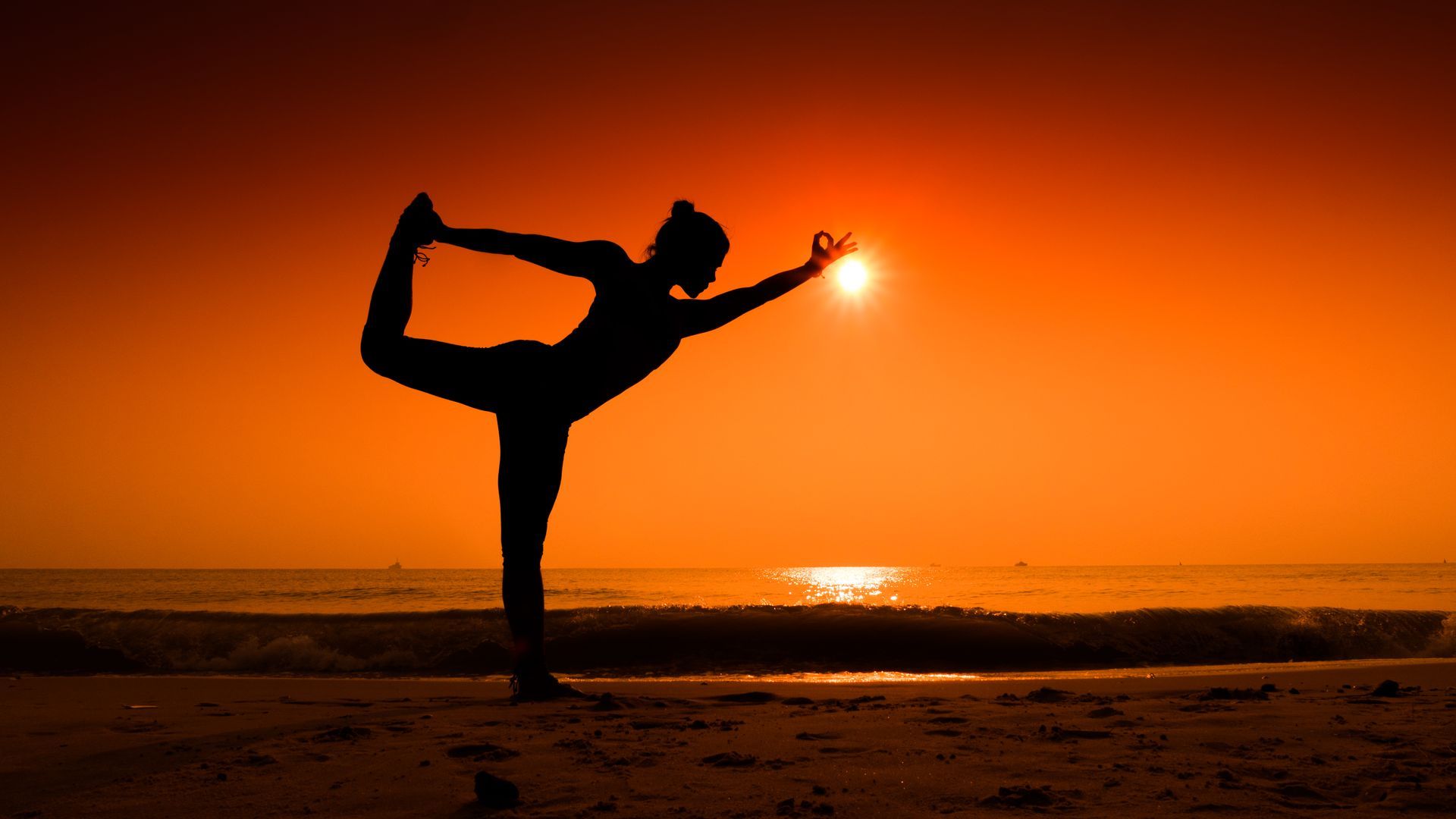 A woman is practicing yoga on the beach at sunset