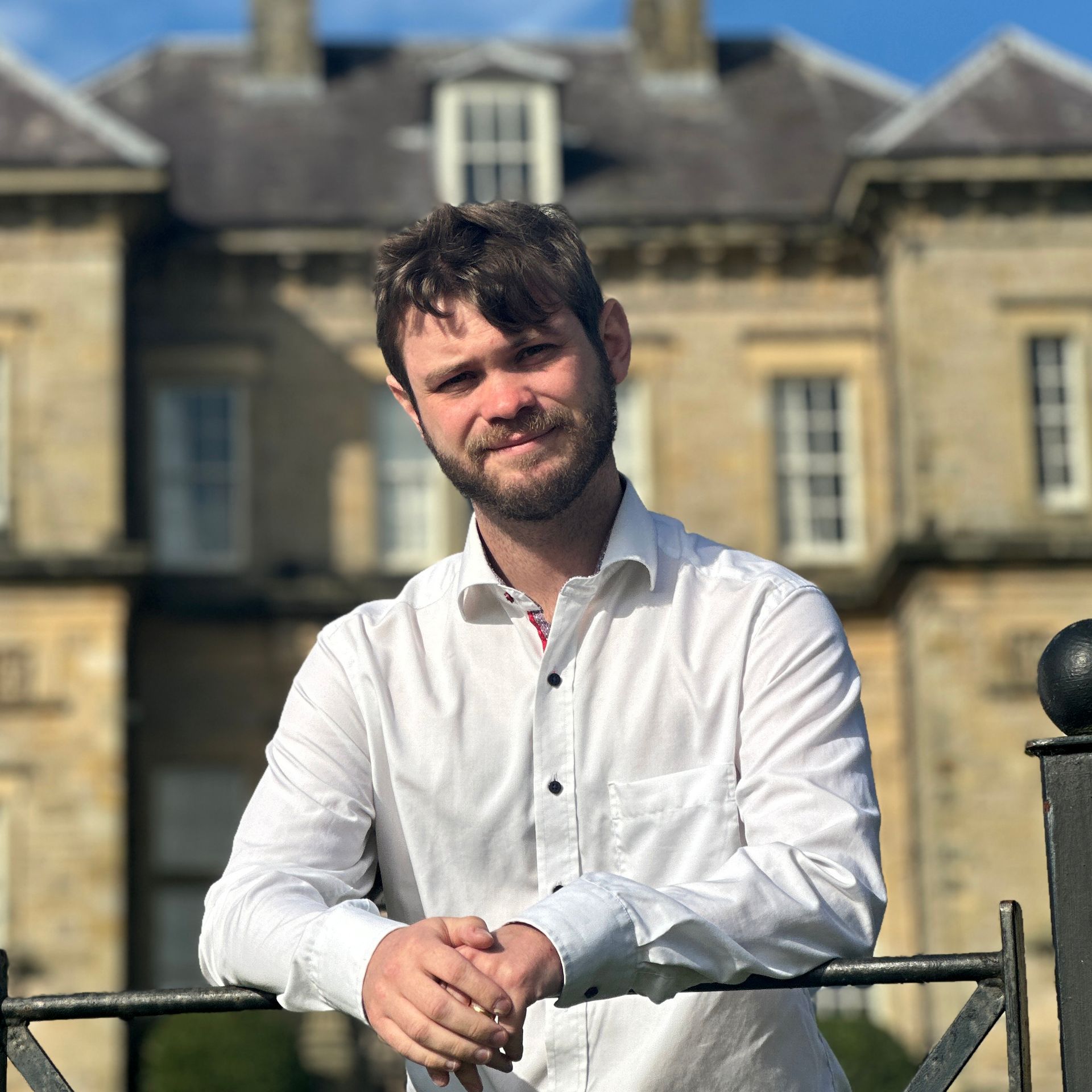 A man in a white shirt is leaning on a railing in front of a large building