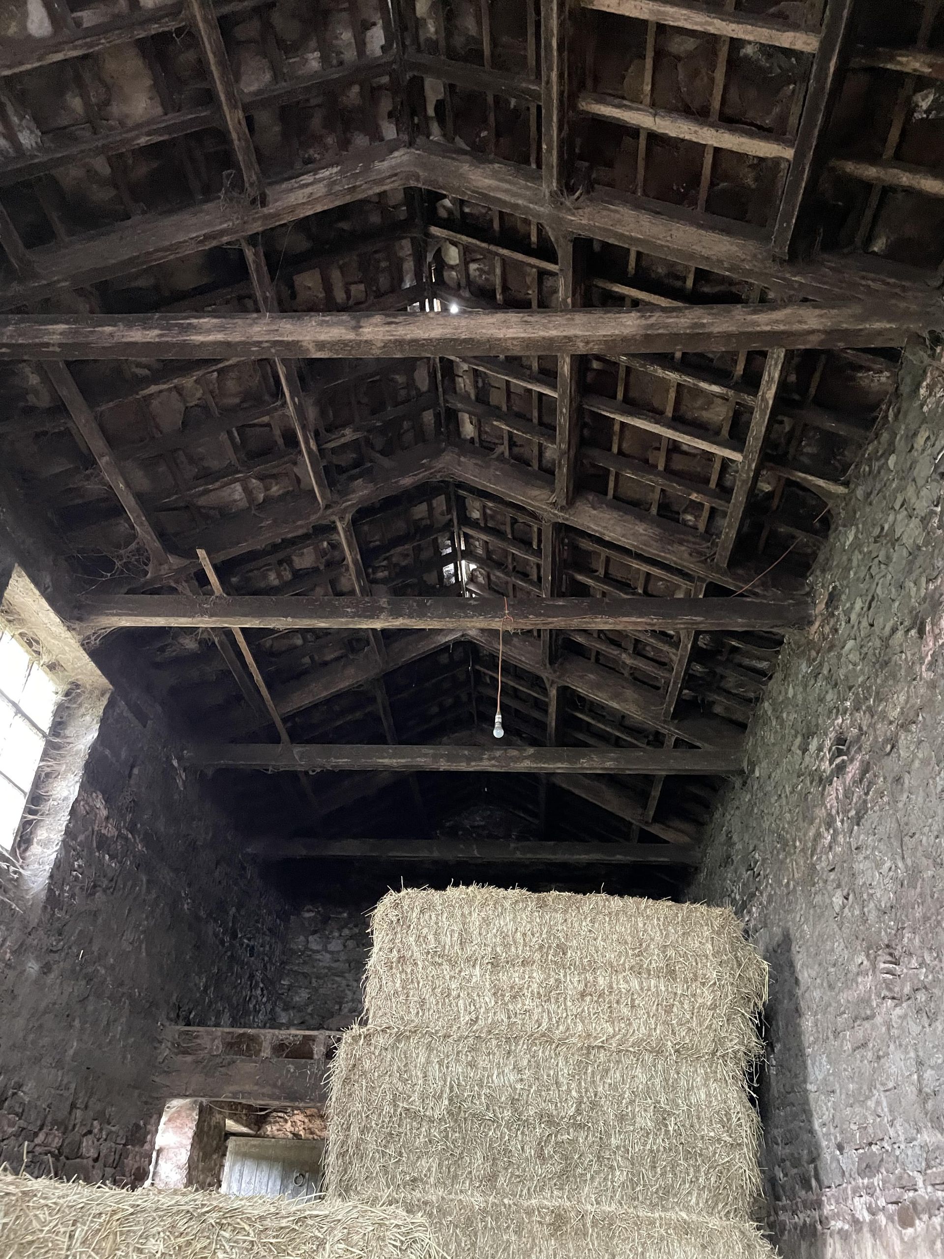 A pile of hay is sitting under a wooden roof in a barn.
