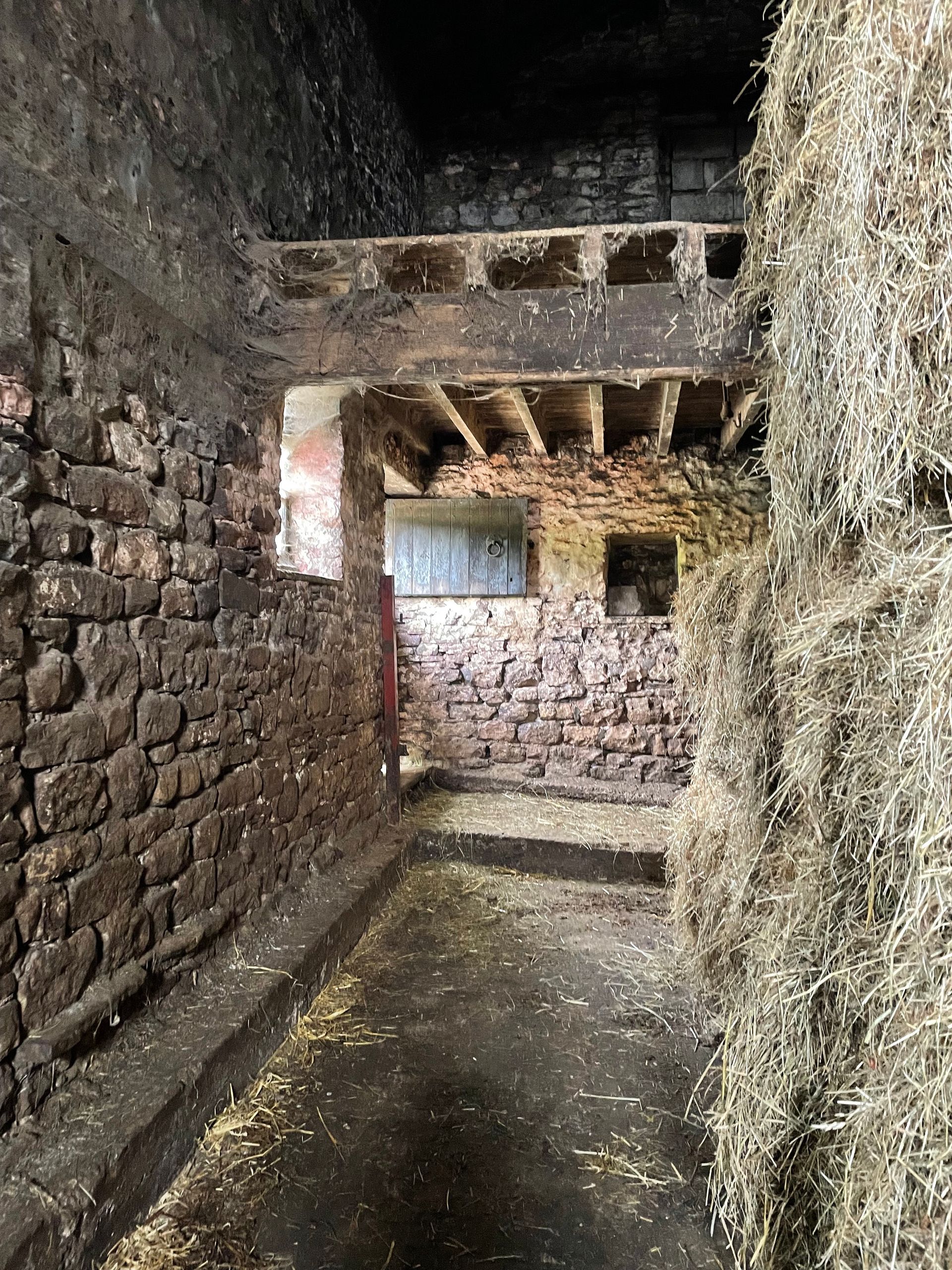 A barn filled with hay bales and brick walls.