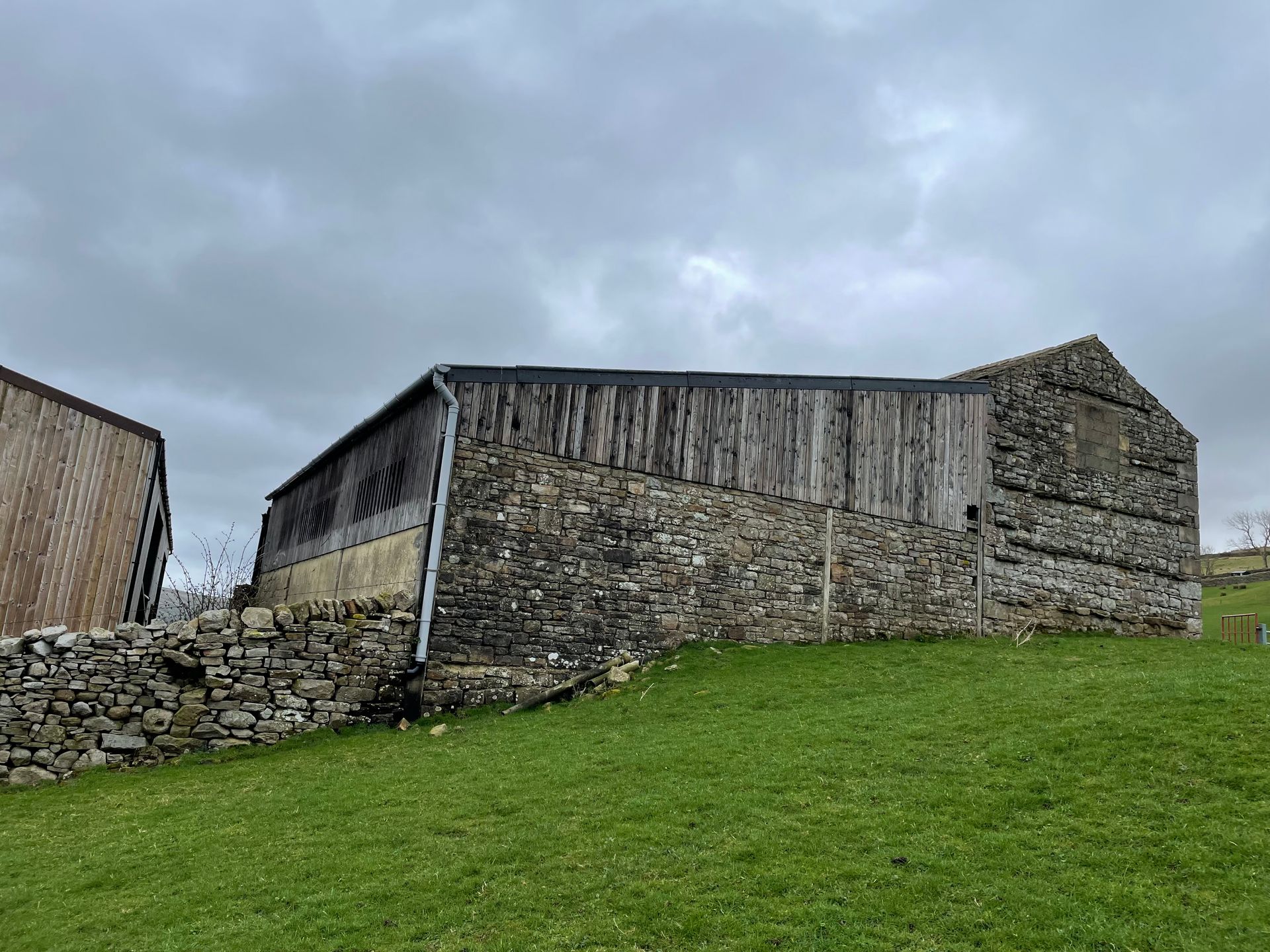A stone barn is sitting in the middle of a grassy field.