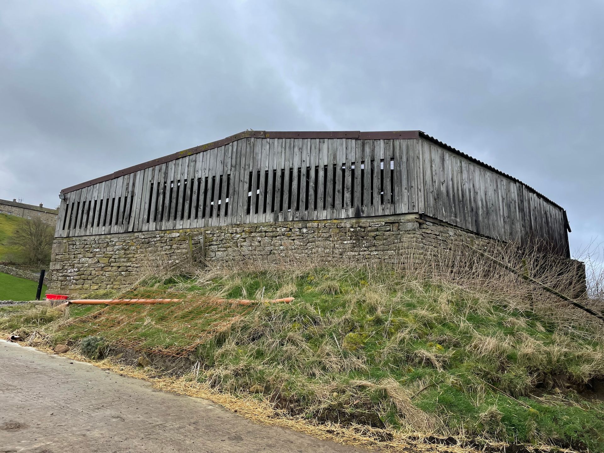 An old barn is sitting on top of a hill next to a road.