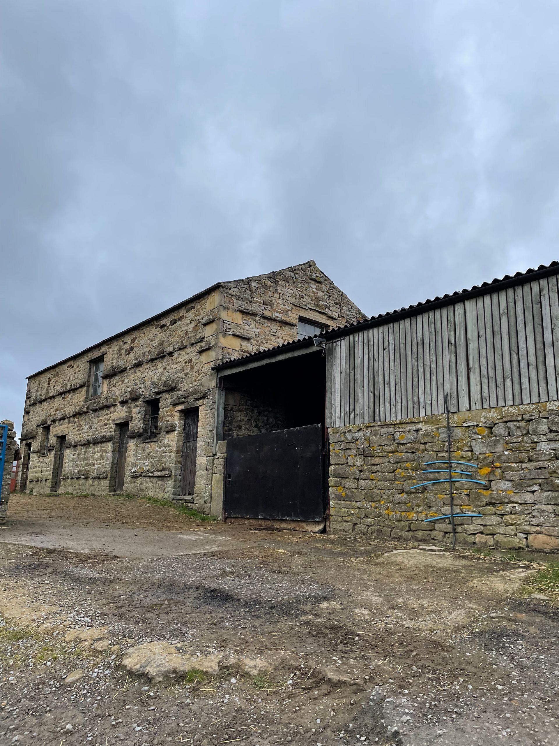 A large stone building with a wooden roof is sitting in the middle of a dirt field.
