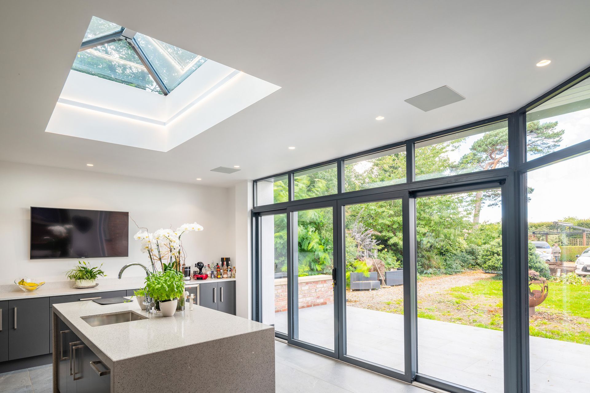 A kitchen with a large island , sliding glass doors , a skylight and a flat screen tv.