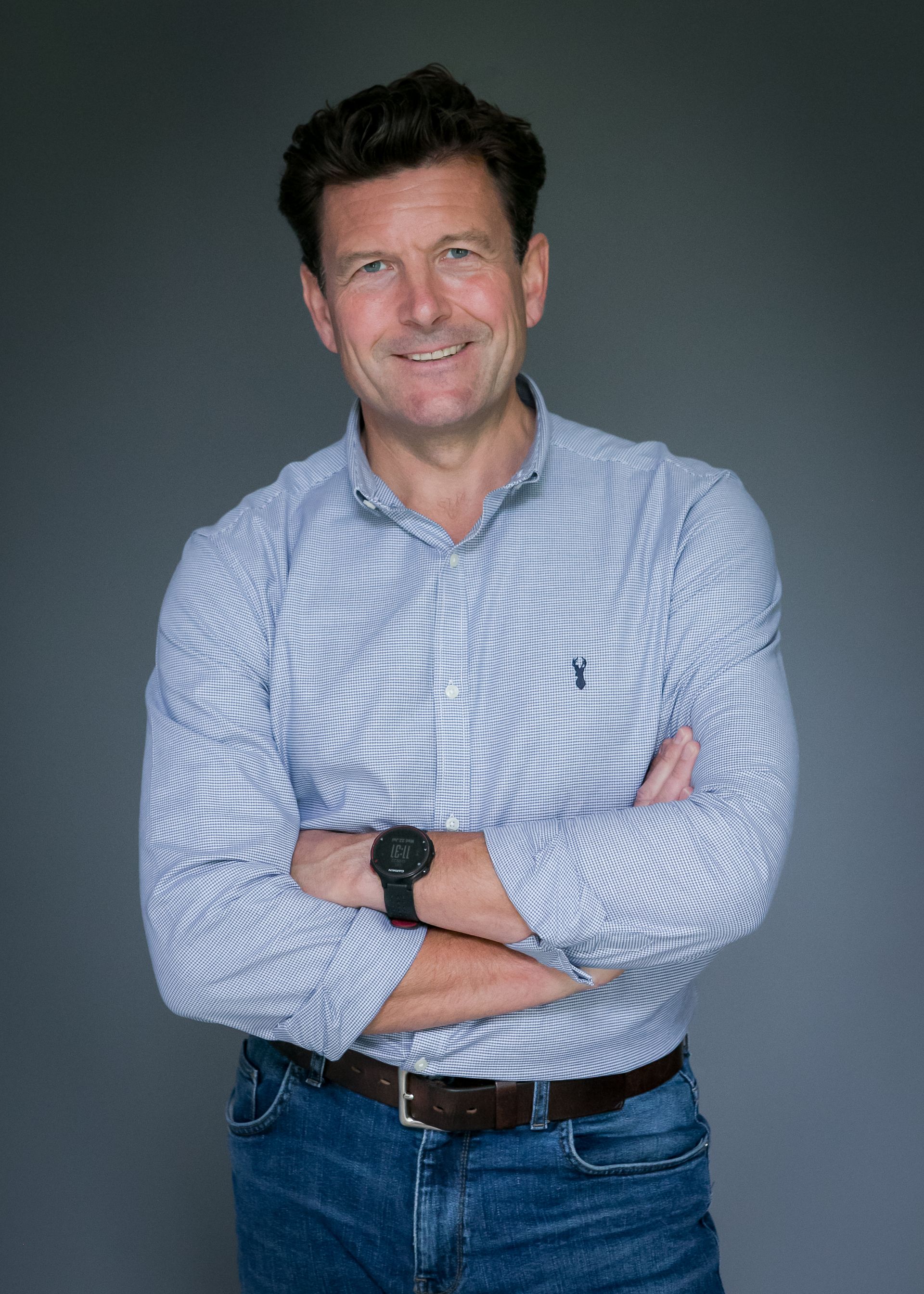 A man in a plaid shirt and jeans is standing with his arms crossed.