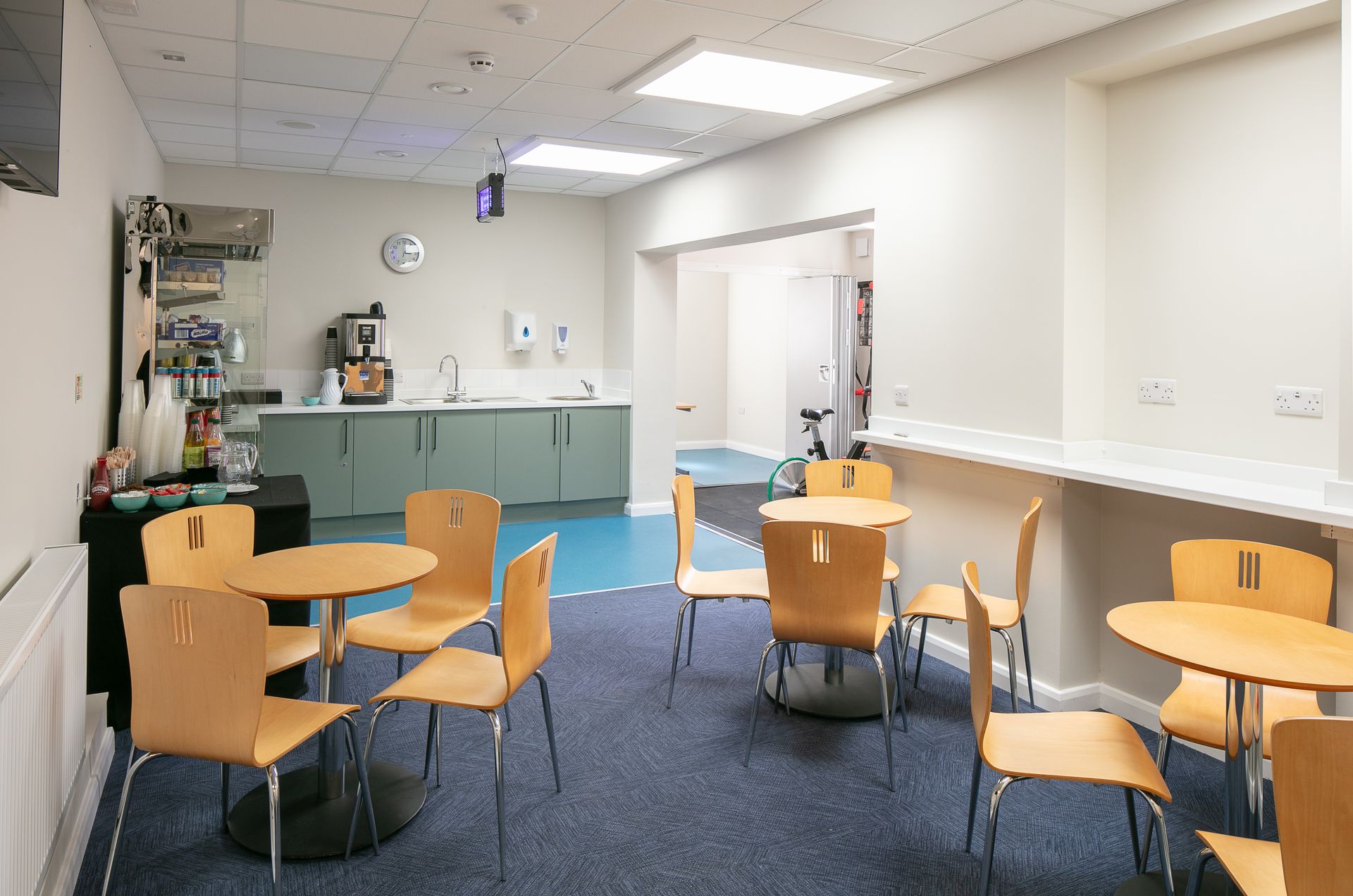 A room with tables and chairs in it and a kitchen in the background.