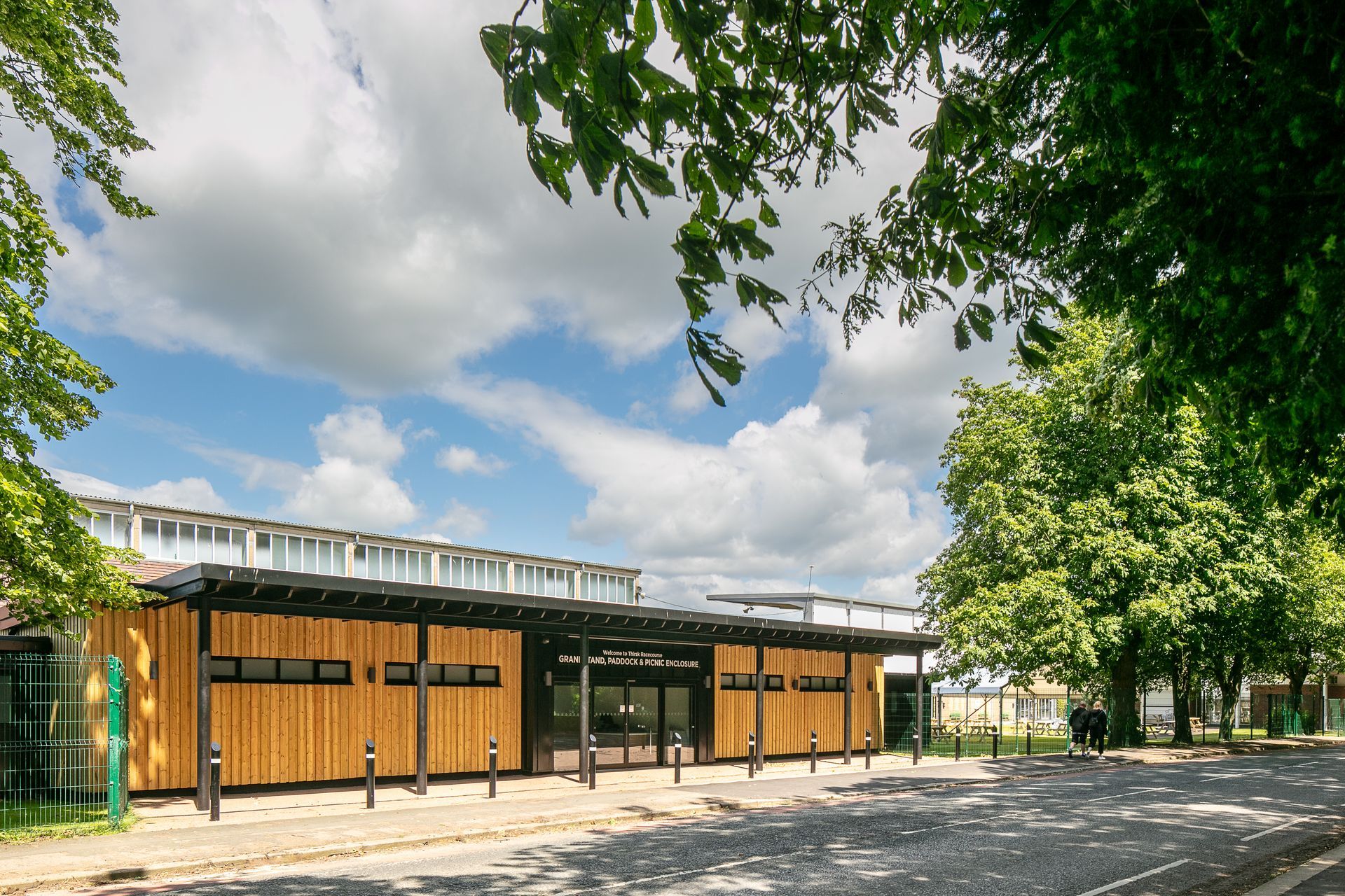 A large building with a wooden facade is surrounded by trees on a sunny day.