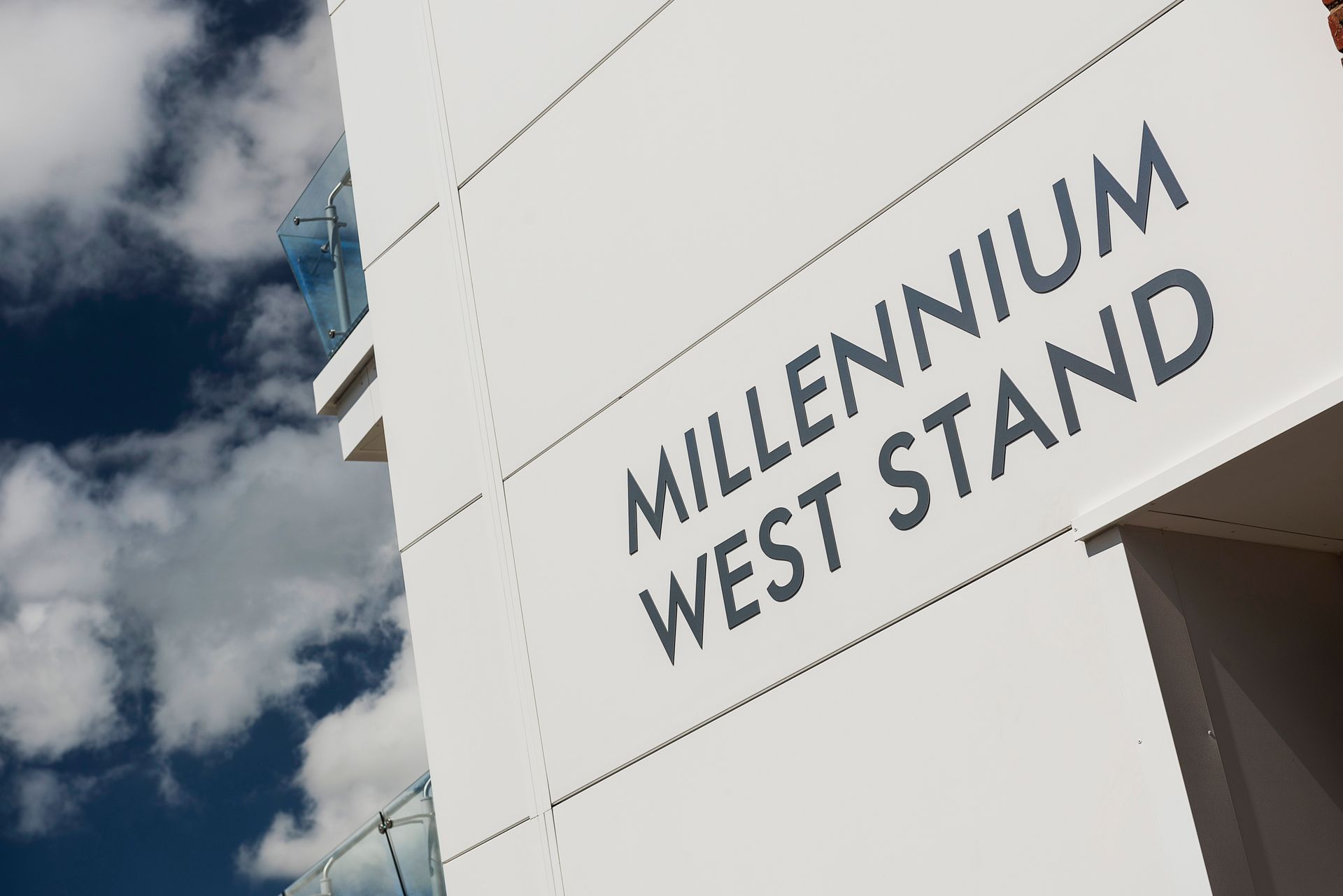 A white building with a sign that says millennium west stand