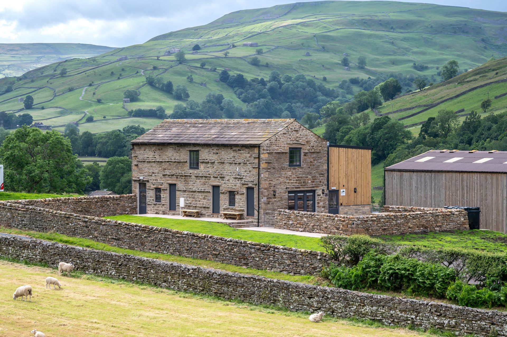 A stone house is surrounded by a stone wall in the middle of a field.