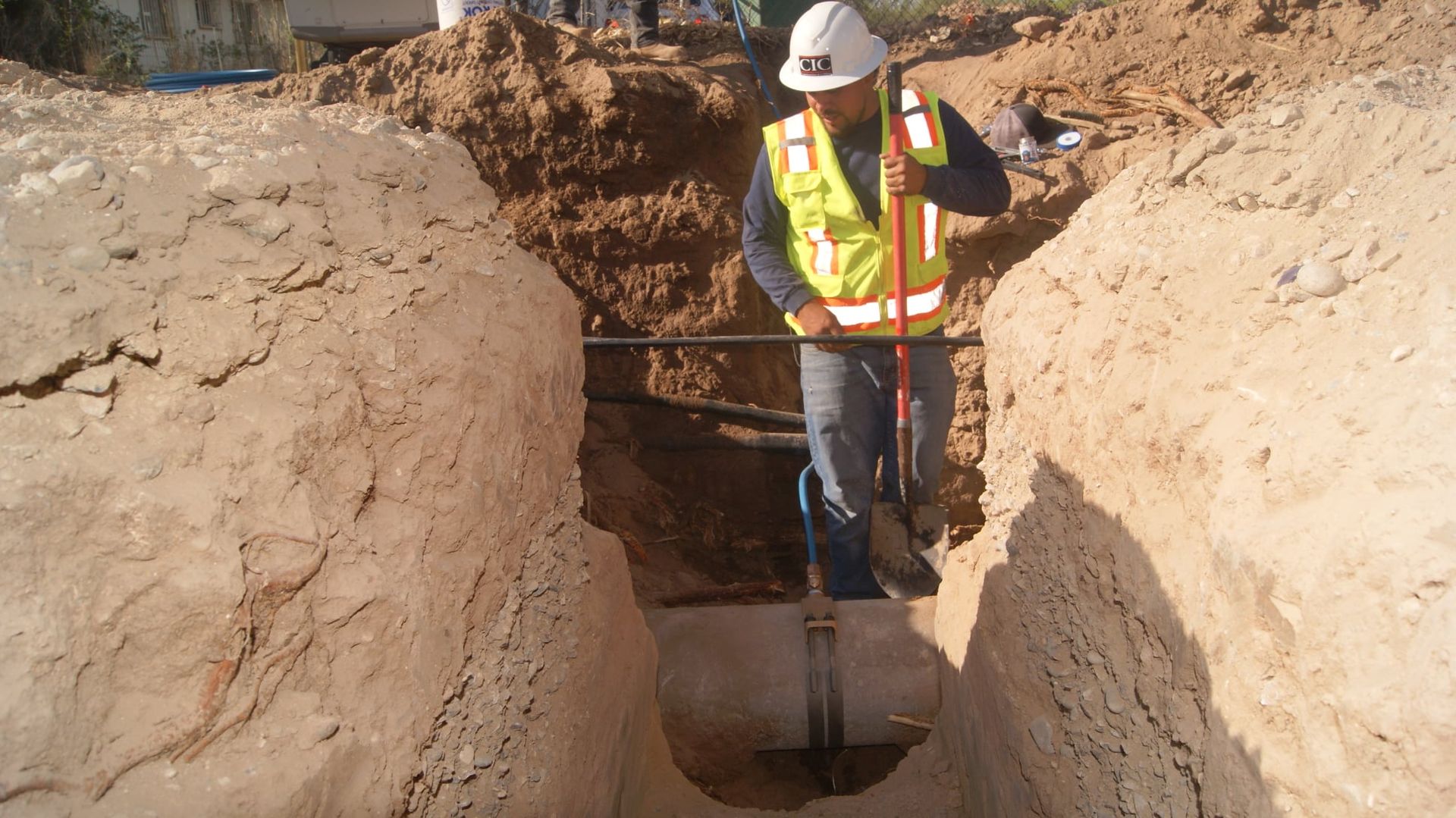 A man wearing a hard hat and safety vest is digging in the dirt