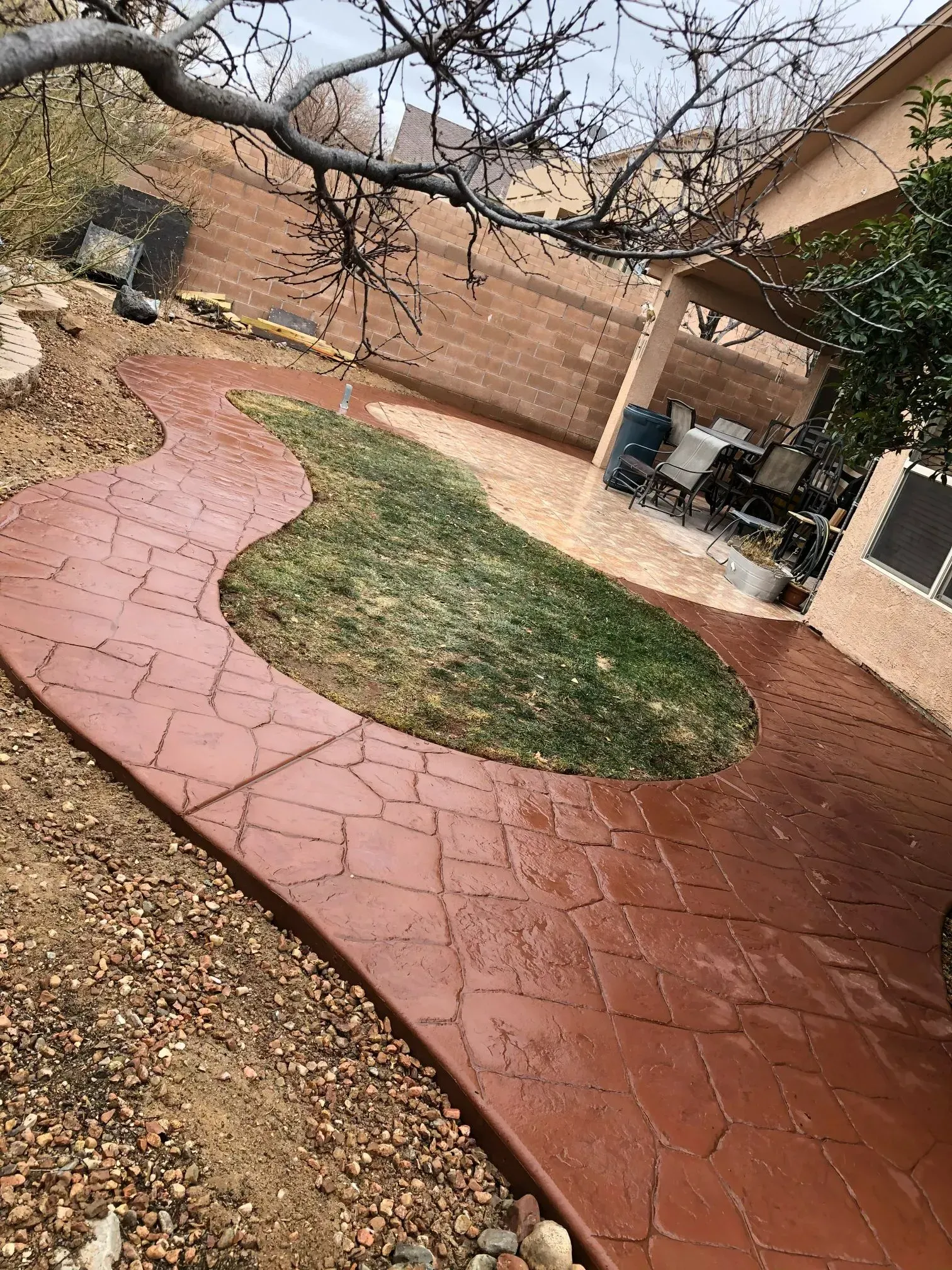 A concrete walkway leading to a patio in a backyard.