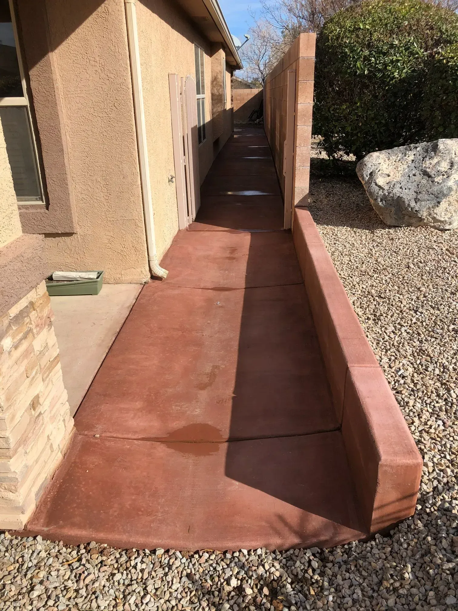 A concrete walkway leading to a house with a brick wall.