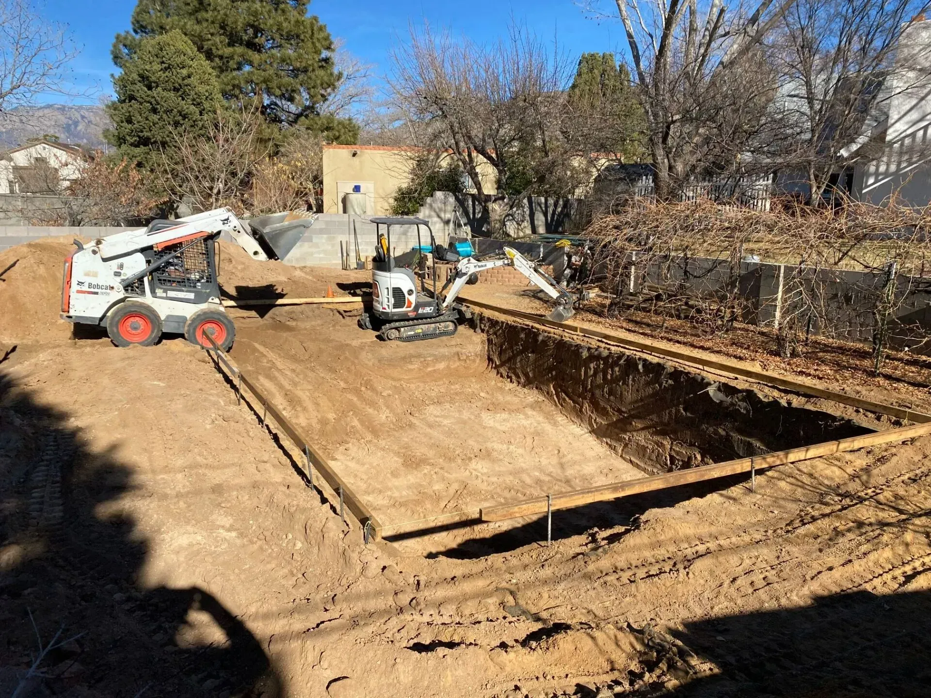 A bobcat is digging a hole in the dirt in front of a house.
