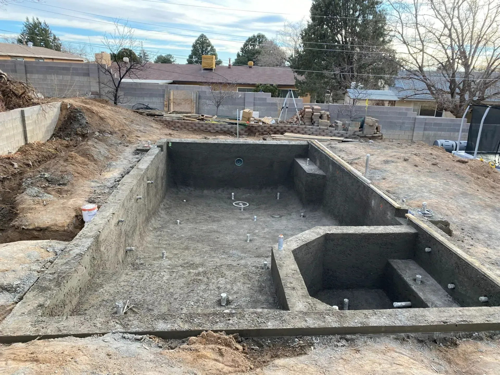 A large concrete pool is being built in a backyard.