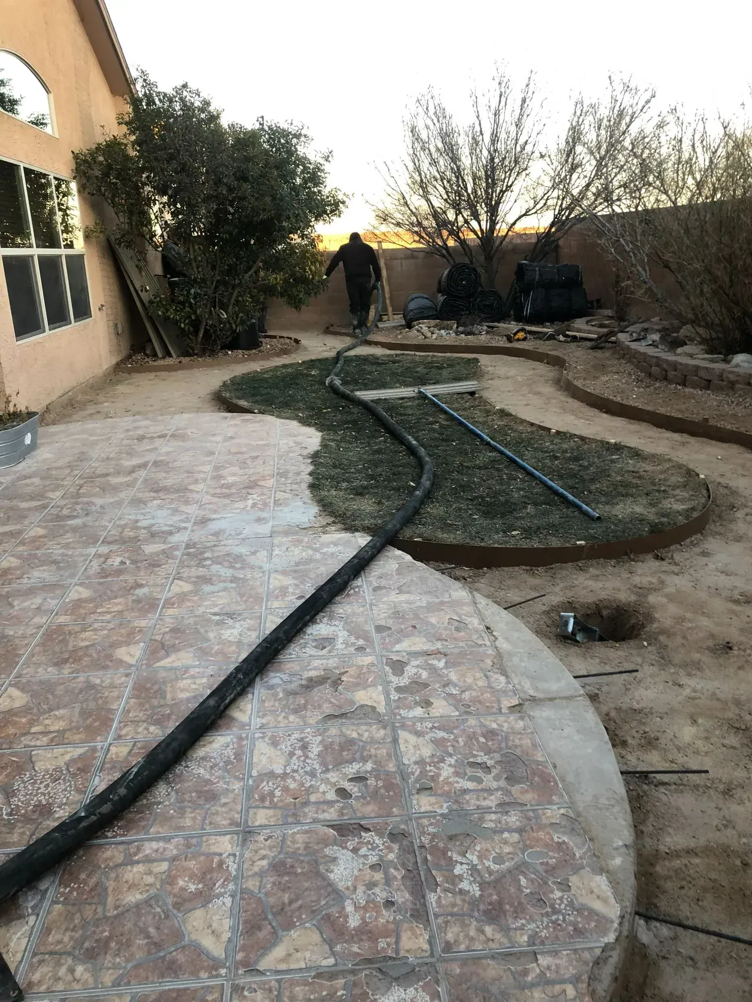 A man is standing in a backyard with a hose.