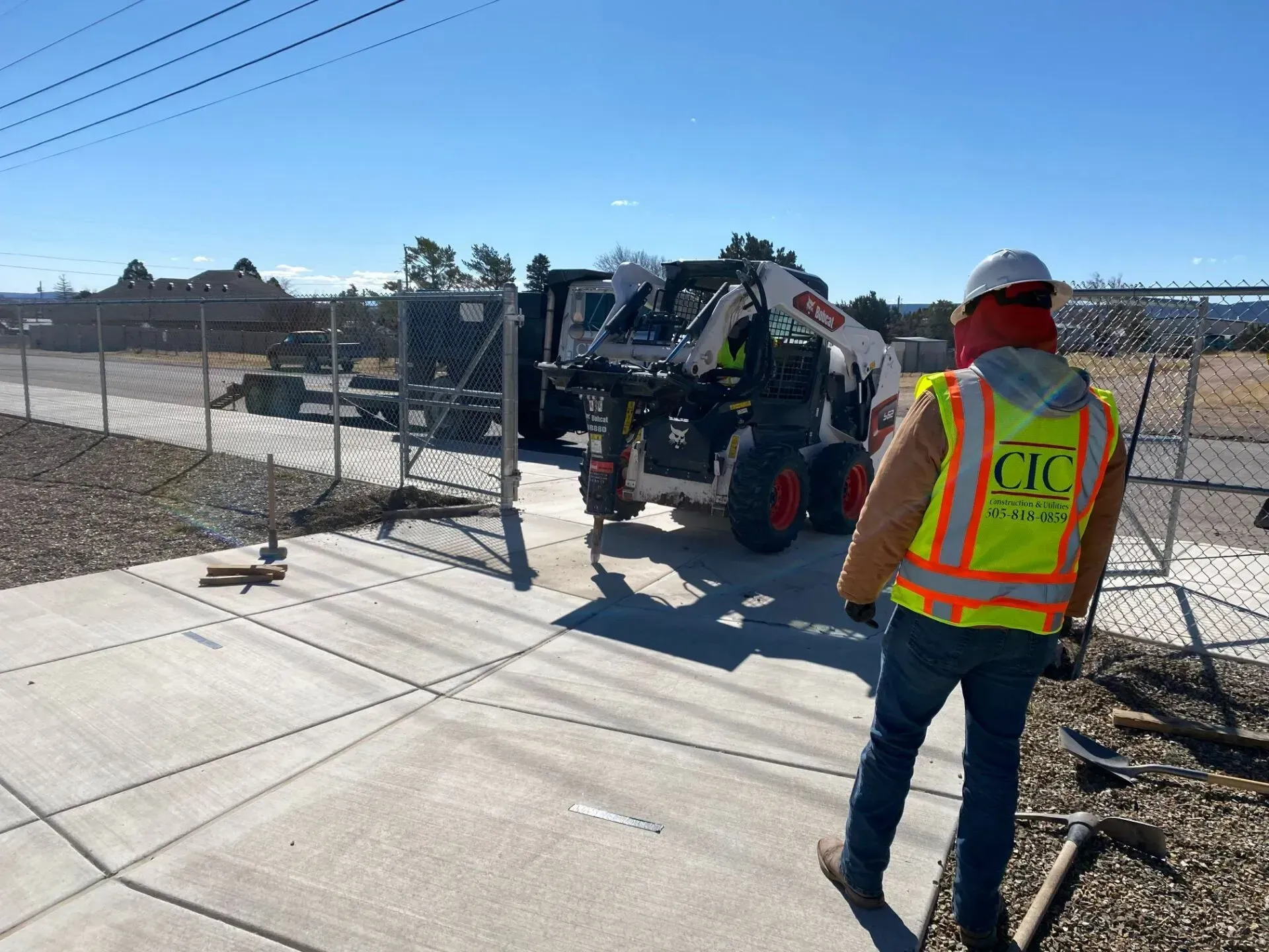 A man in a safety vest is walking towards a bobcat tractor.