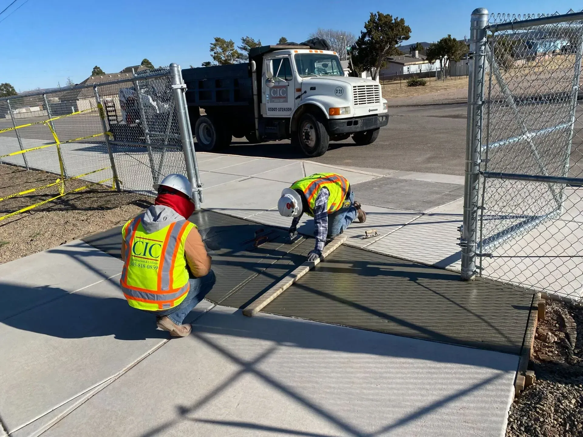 Two construction workers are working on a sidewalk in front of a truck.