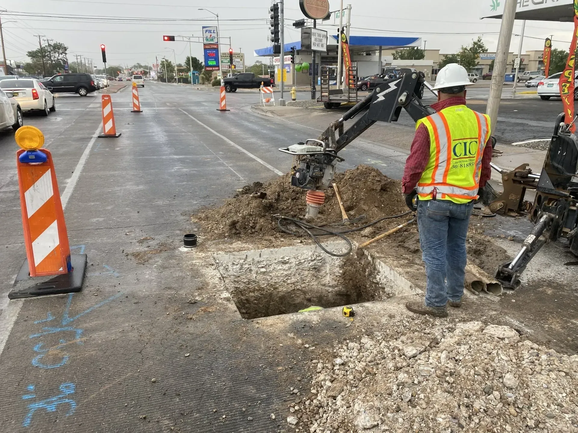 A man wearing a hard hat and safety vest is digging a hole in the ground.