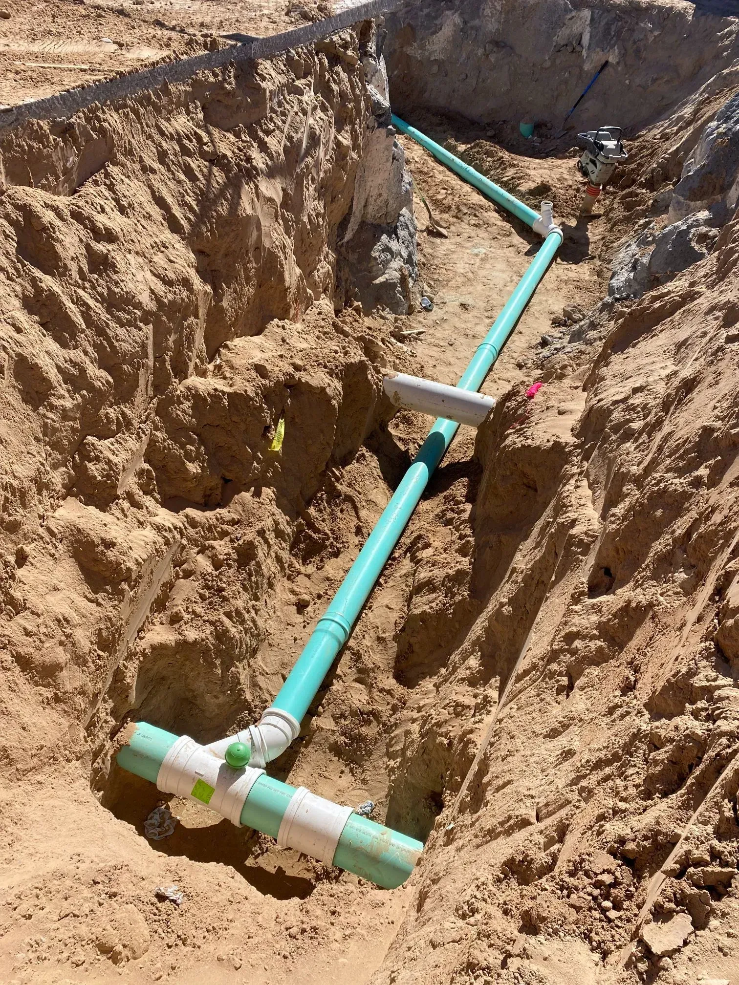 A green pipe is being installed in a hole in the ground.