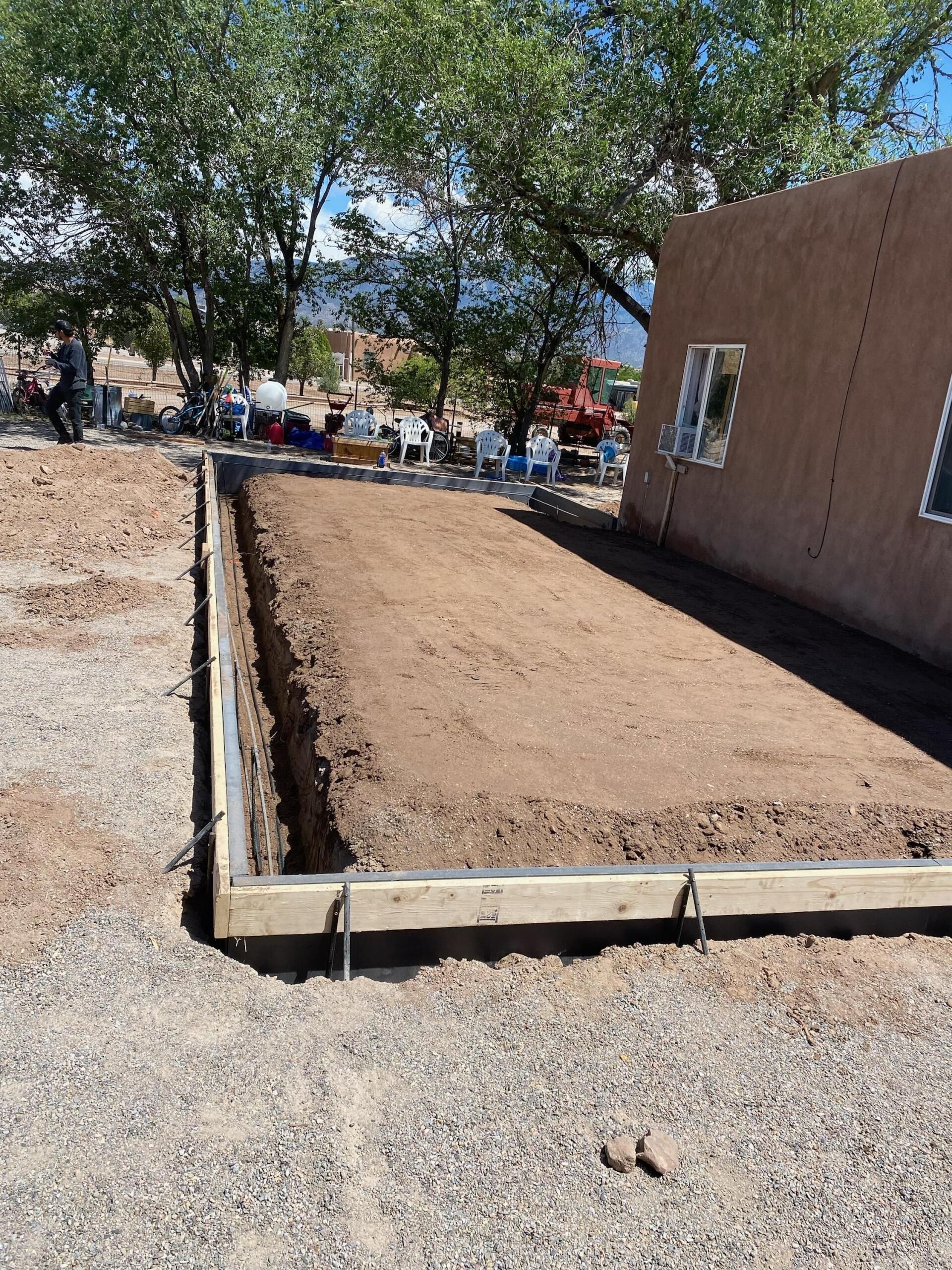 A house is being built on a dirt lot next to a tree.