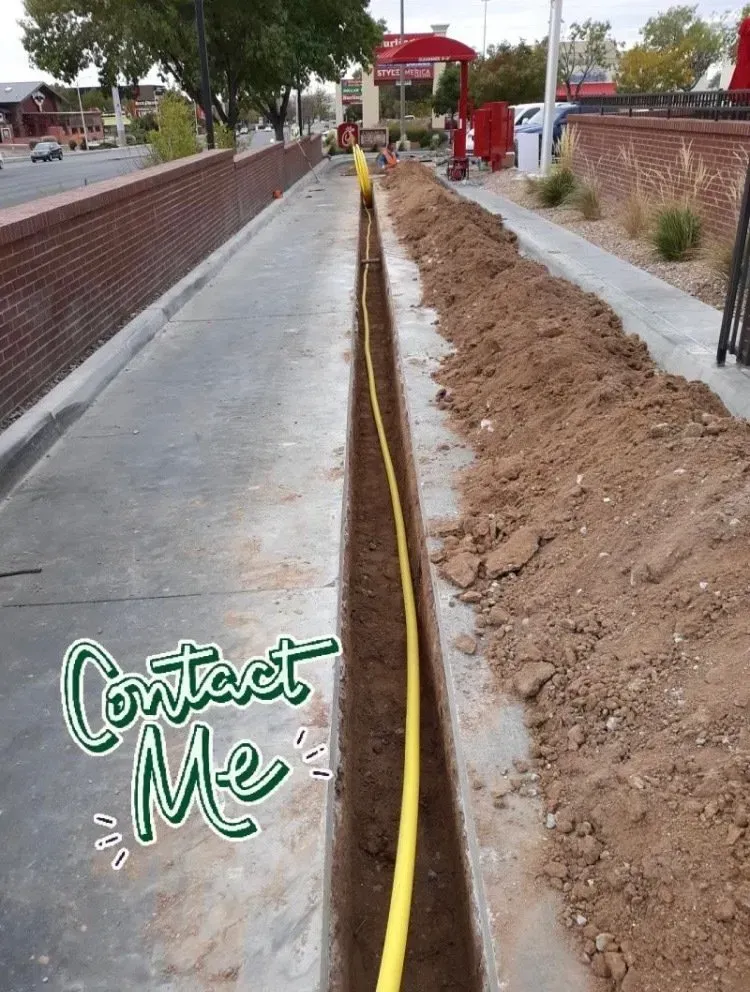 A yellow hose is laying in the dirt next to a sidewalk.
