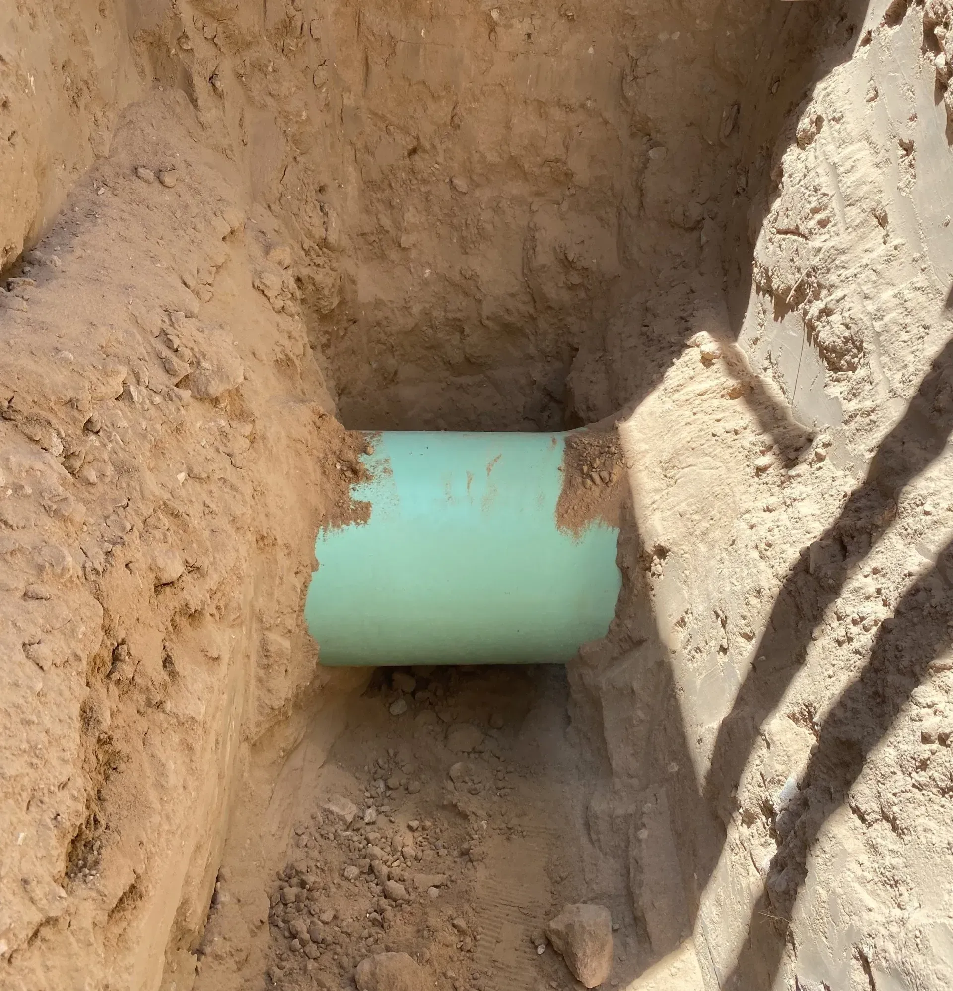 A green pipe is in a hole in the dirt