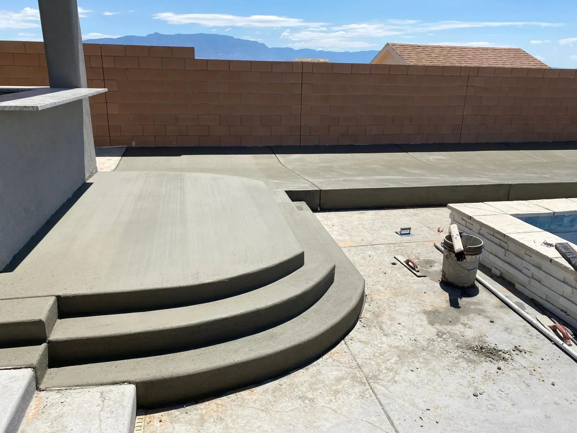 A person is working on a concrete patio next to a pool.