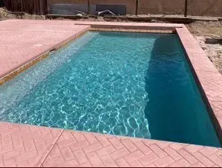 A large swimming pool filled with blue water and a red brick border.