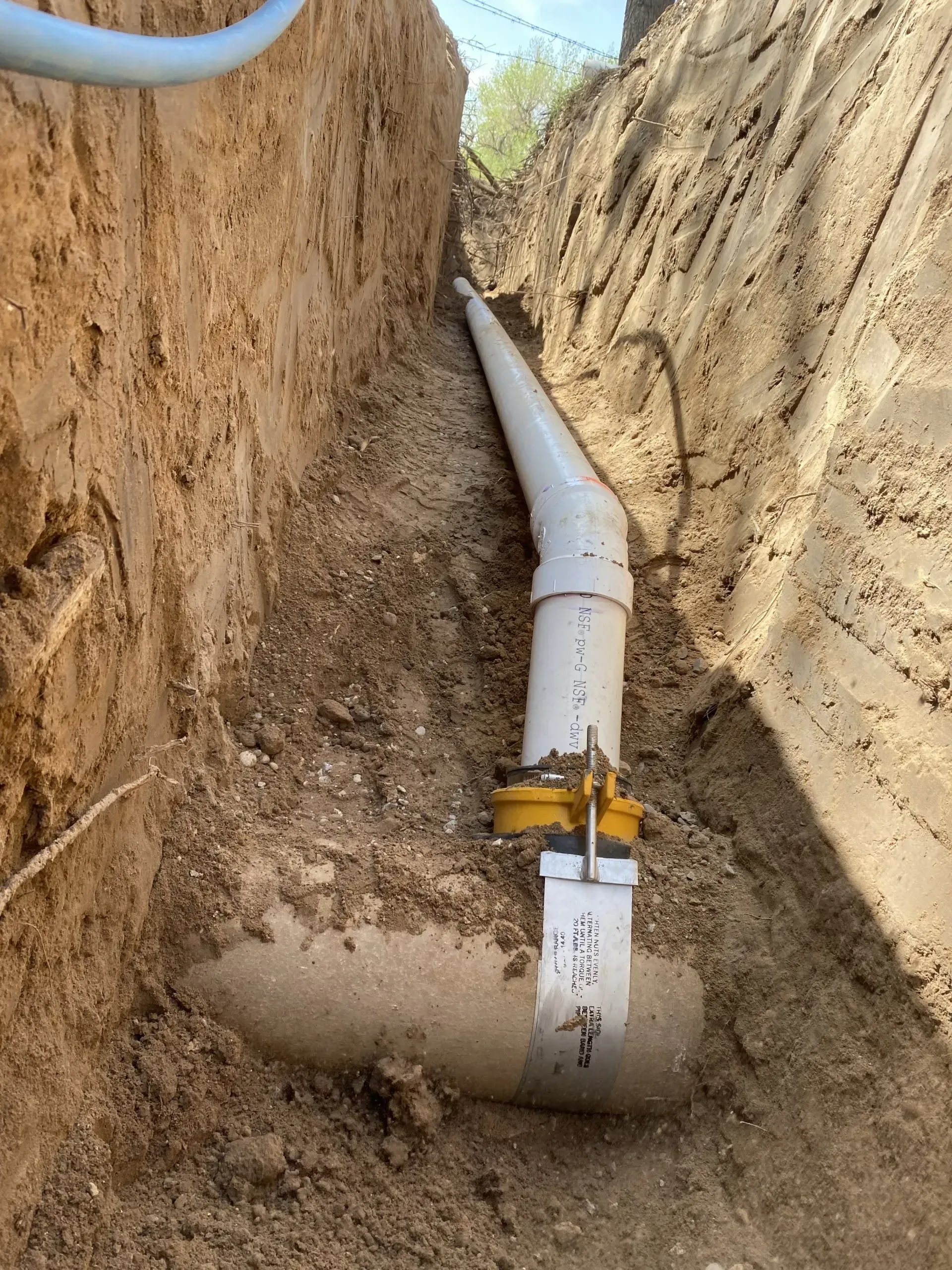A white pipe is laying in the dirt in a trench.