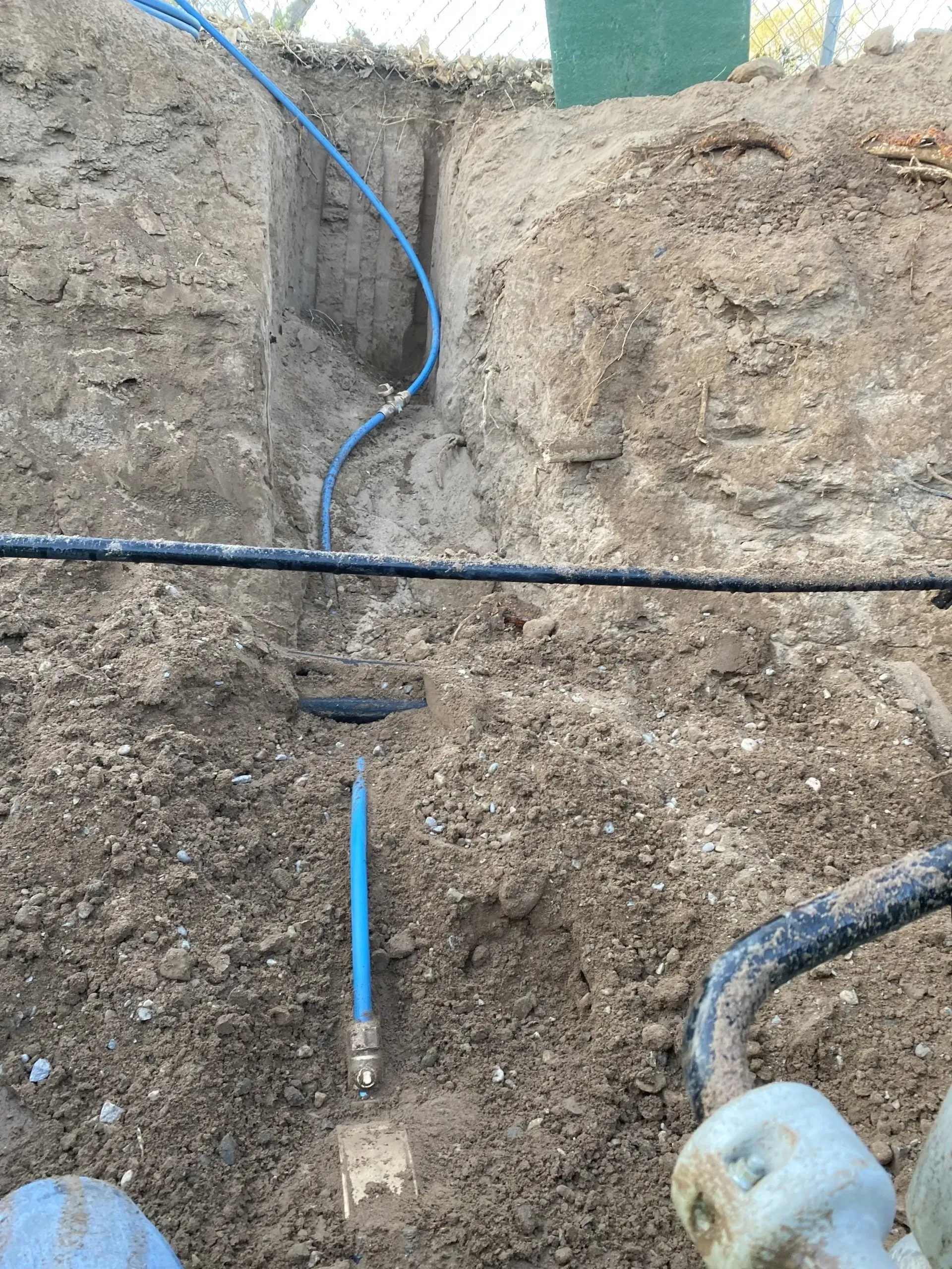 A blue pipe is laying in the dirt next to a black pipe.