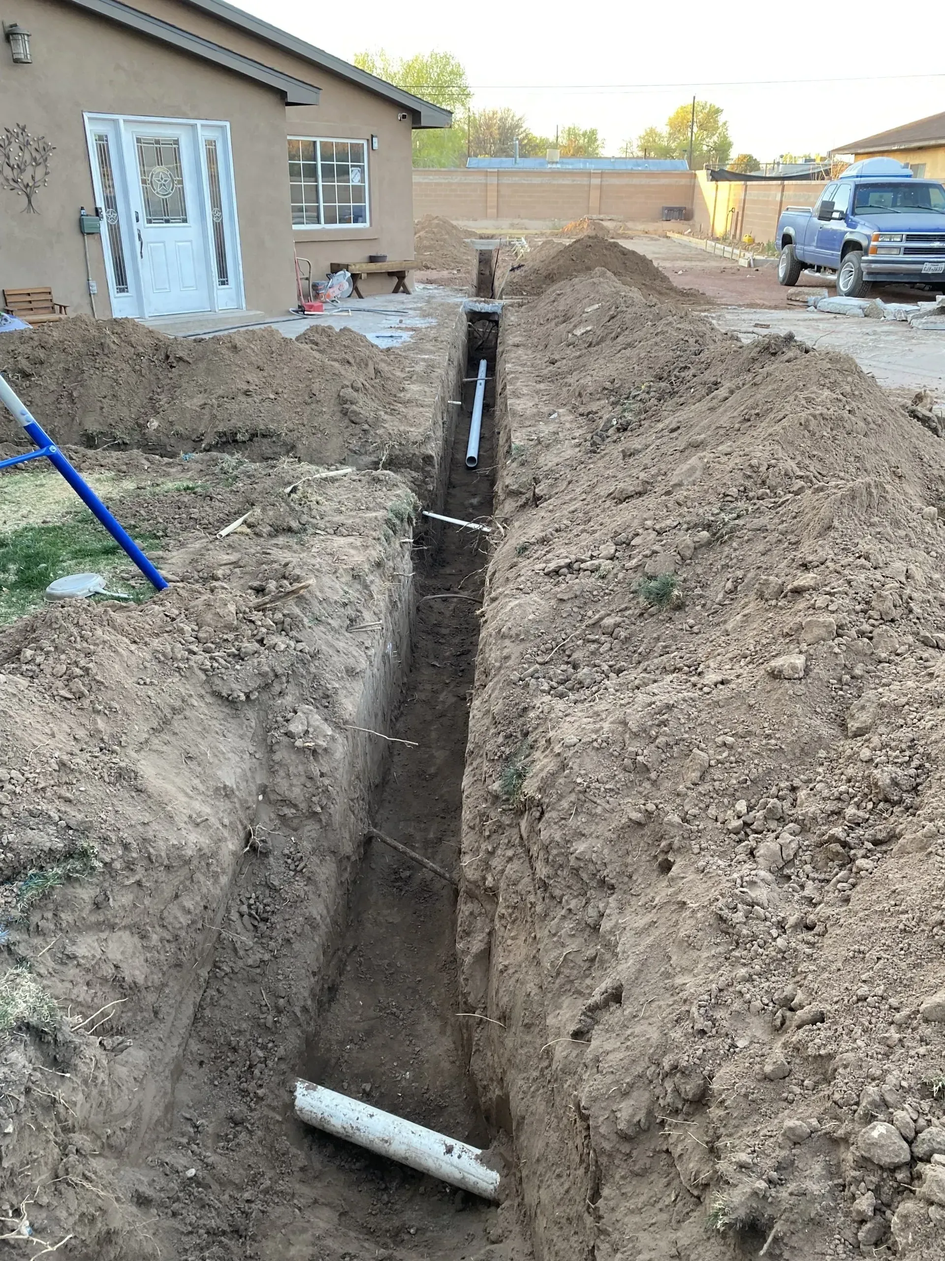 A drain pipe is being installed in a trench in front of a house.
