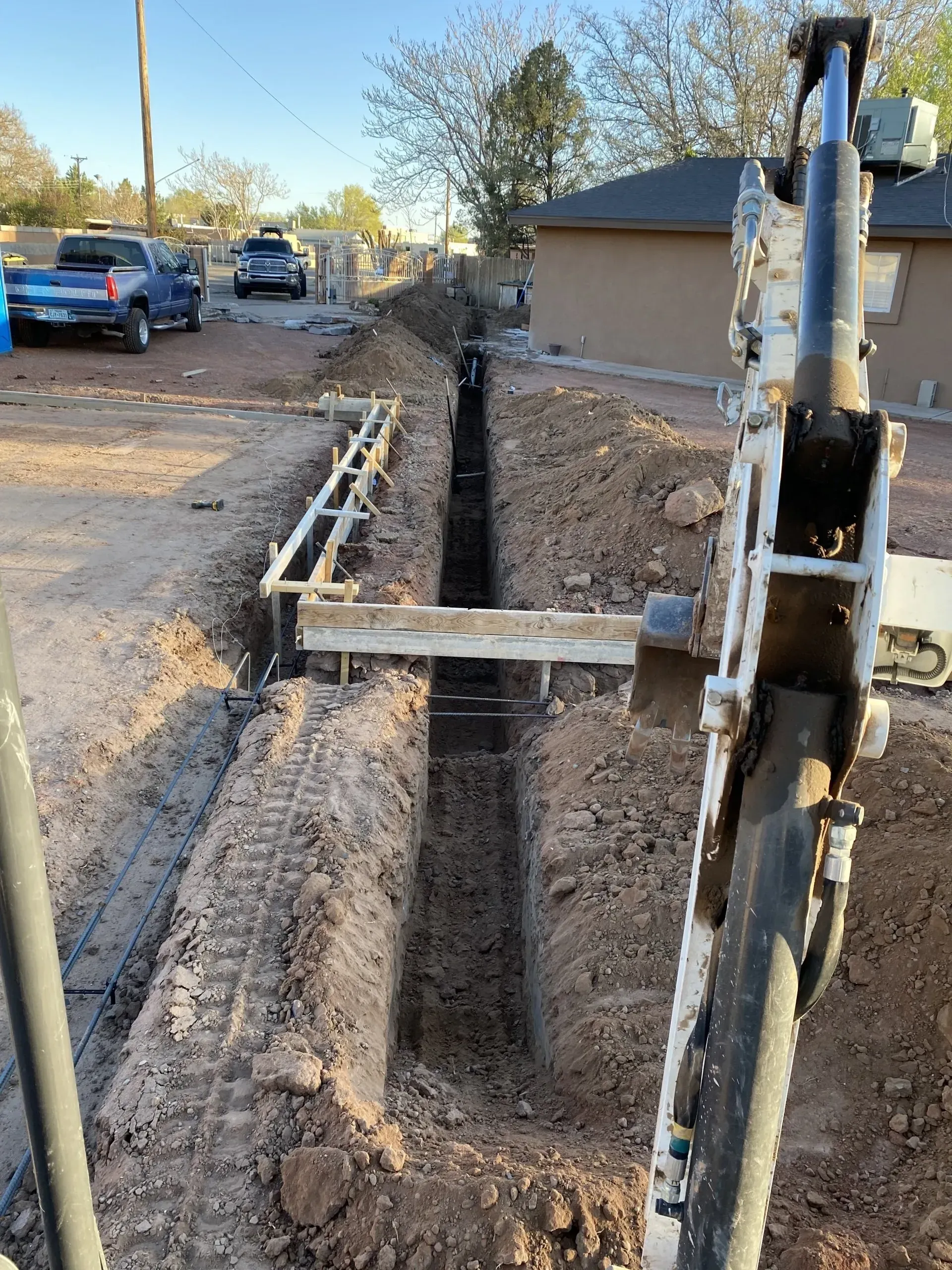 A machine is digging a trench in the dirt next to a house.