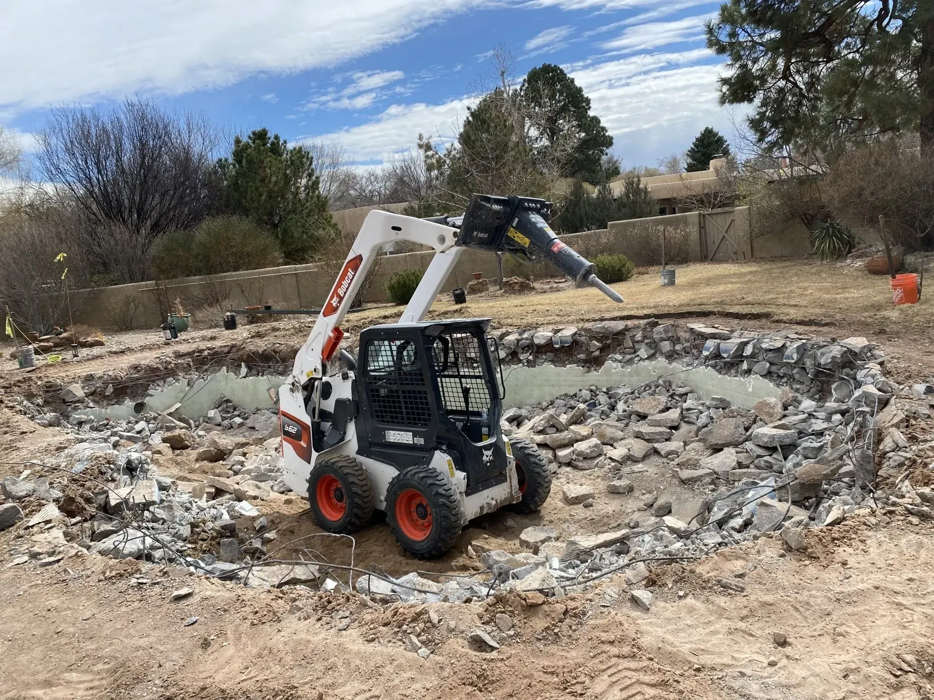 A bobcat is driving through a pile of rocks in a dirt field.