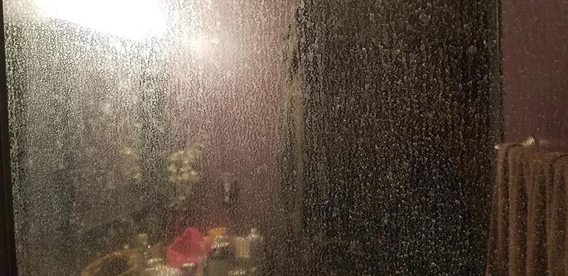 A close up of a shower door with water drops on it in a bathroom.