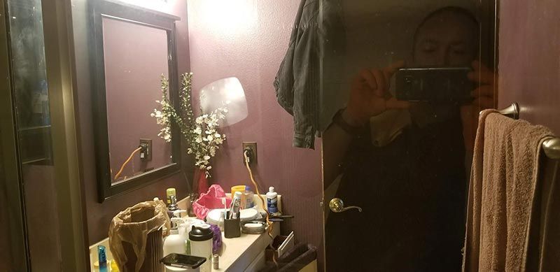 A bathroom with a sink , mirror , and towels . a person is taking a selfie in the mirror.
