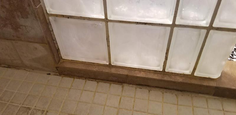A bathroom with a glass block shower door and tile floor.