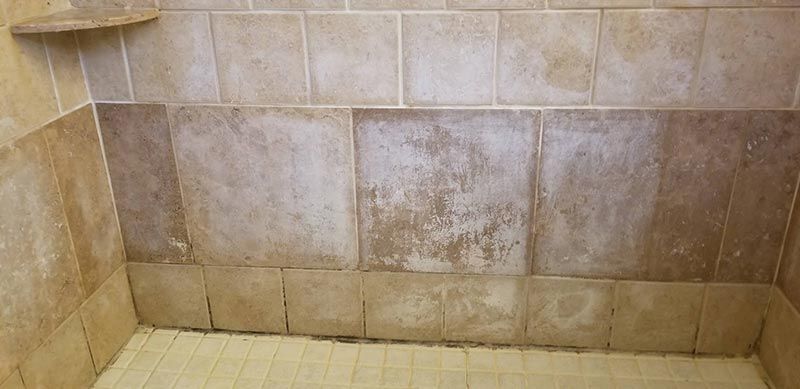 A bathroom with a tiled shower wall and a tiled floor.