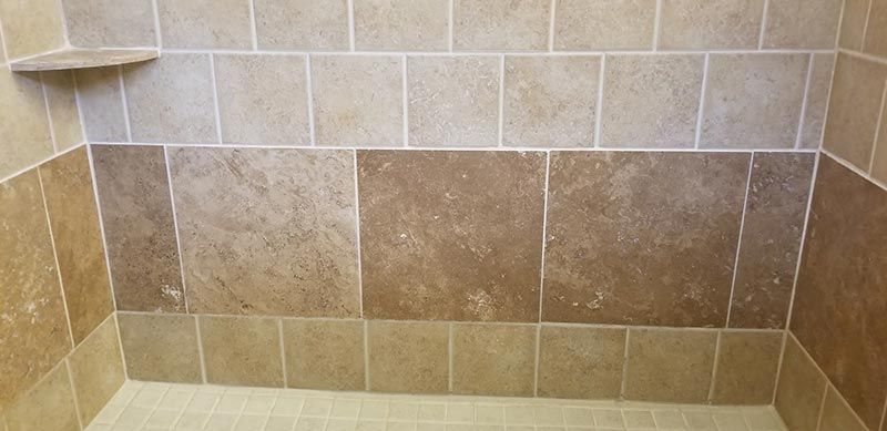 A shower stall with brown tiles and a shelf.