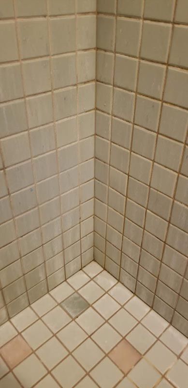 A corner of a bathroom with white tiles and a pink floor.
